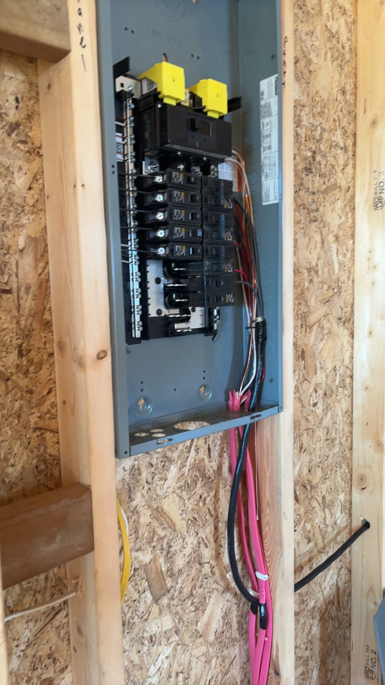 An electrical breaker panel installed in a wooden wall with various circuit breakers and wiring.