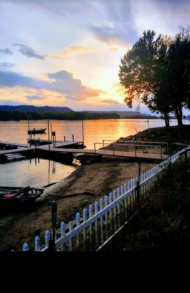 Sunset over the Mississippi River with green bluffs in the background and boat docks in the foreground.