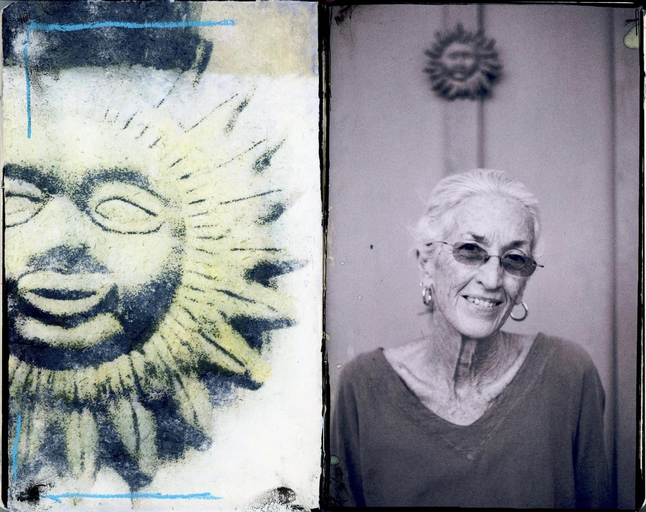 A black and white photo of an elderly woman with white hair wearing sunglasses, earrings, and a dark top, standing in front of a plain wall with a decorative sun-shaped ornament. Next to her is a spray-painted image of a smiling sun.