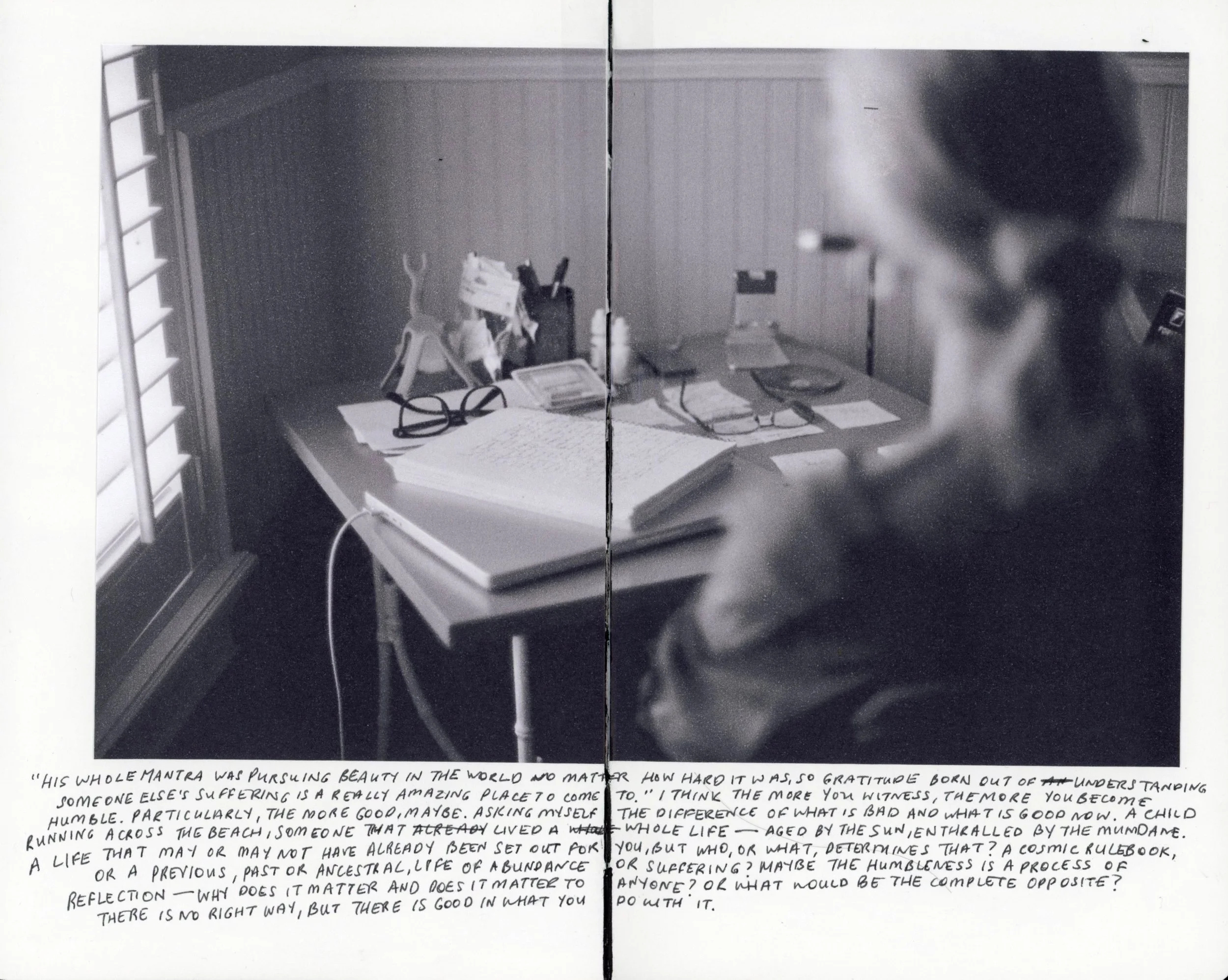 A desk with glasses, papers, a telephone, and children's toys, viewed from the side with a person with glasses in the foreground, near a window with blinds.