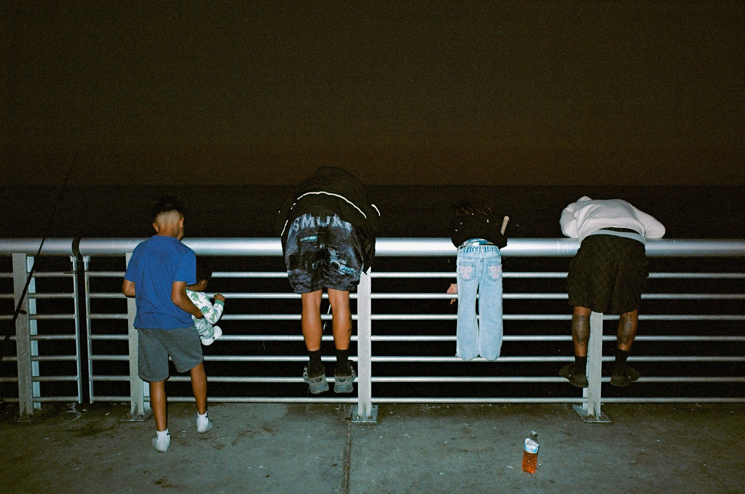 Four young people leaning over a pier railing at night, looking at the water.