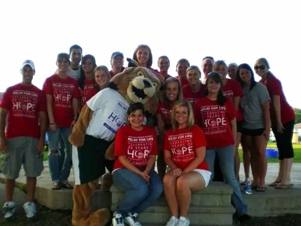 Kim Kohlhepp with the Ohio University Relay for Life Planning team. Group of people with a mascot lion in the center, outdoors on steps, some wearing red shirts with awareness message.