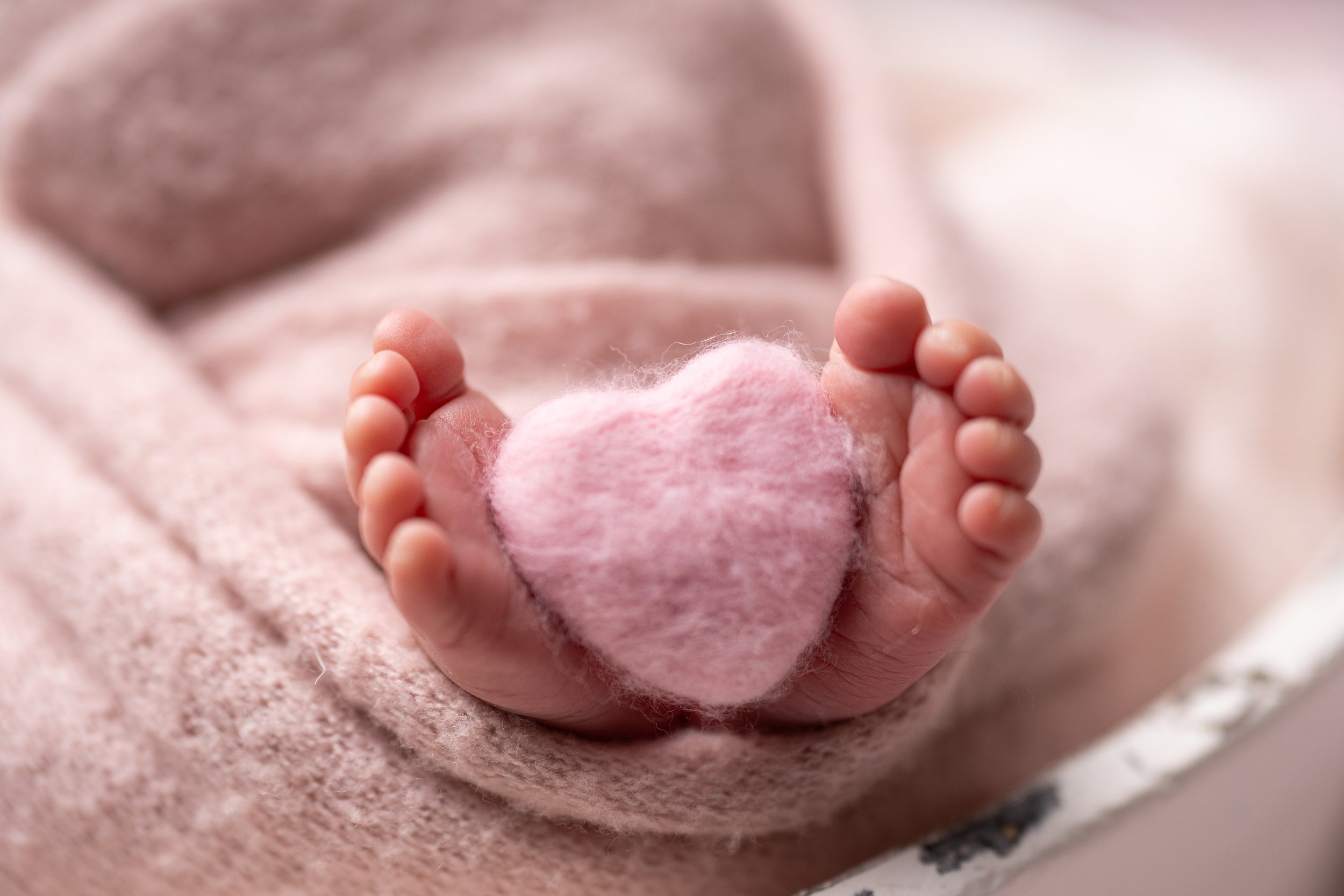 Close-up of tiny baby hand holding a pink, fluffy heart-shaped object.