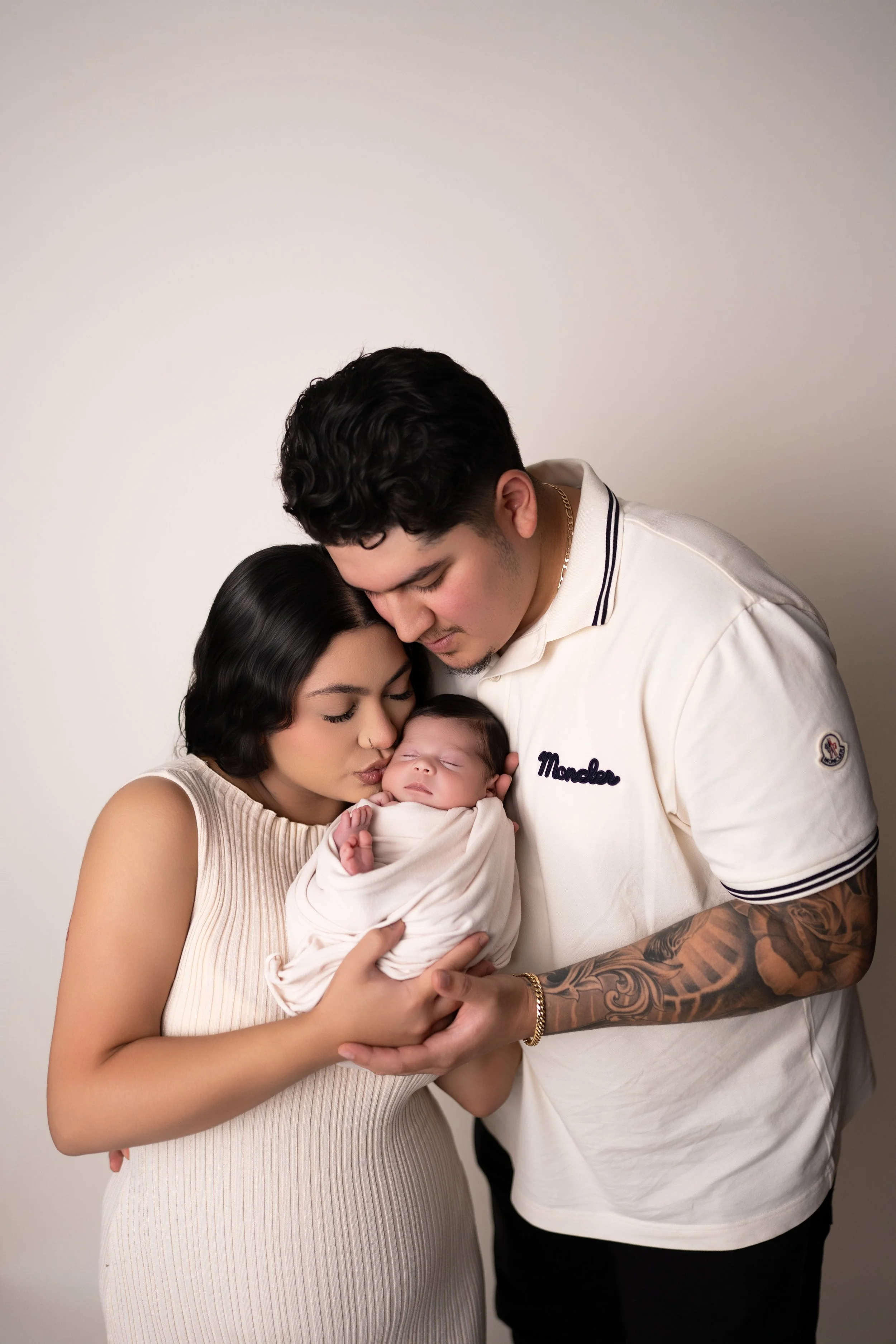 A young family of three in a warm embrace, with the mother and father tenderly holding their newborn baby.