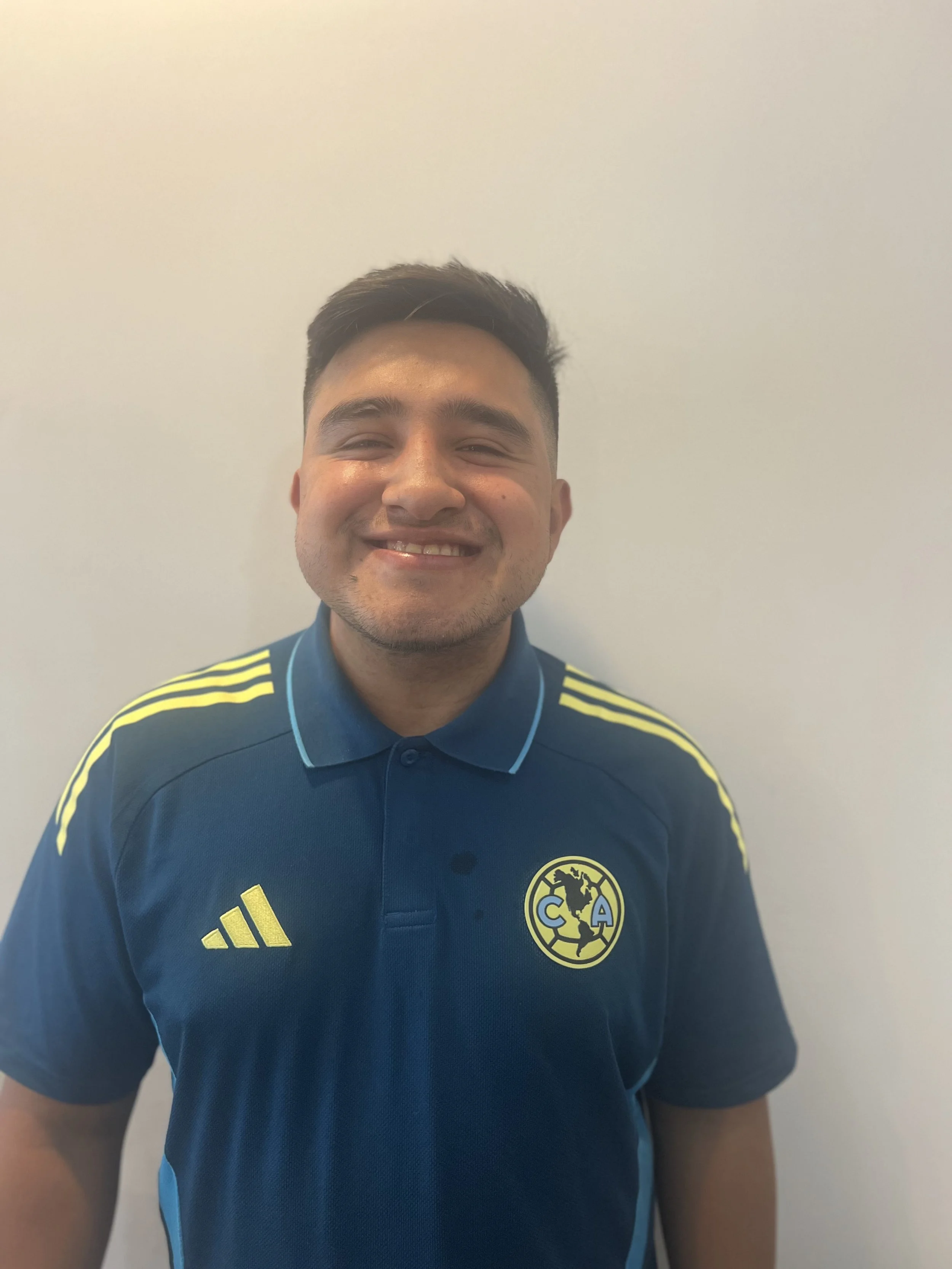 Hombre sonriendo con camiseta del Club América en fondo blanco.