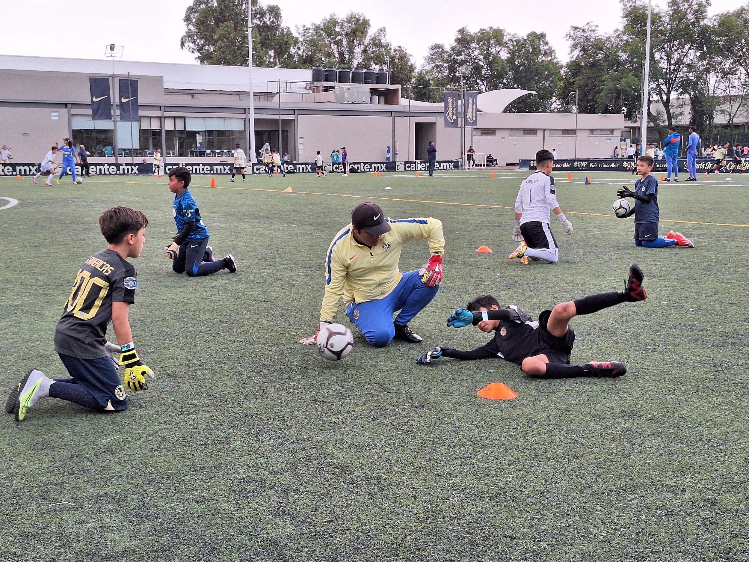 Niños y jóvenes entrenando en un campo de fútbol, algunos con guantes de portero, en un entrenamiento o práctica.