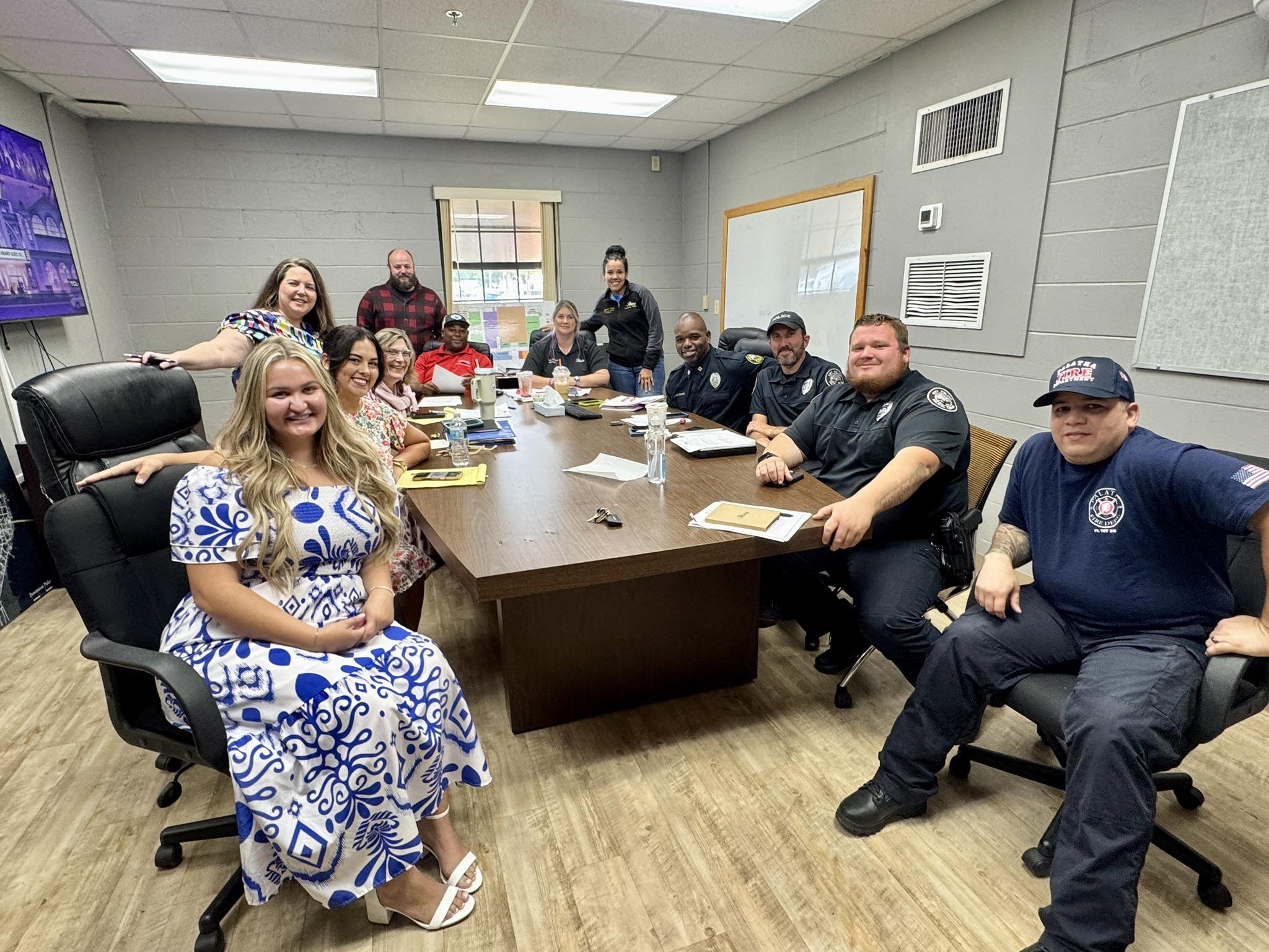 A group of thirteen people, including emergency responders and civilians, gathered around a conference table in a meeting room, smiling for the photo.