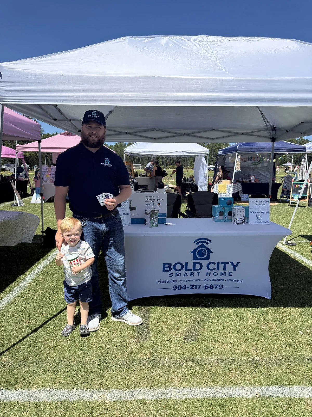 Brandon Eichhorn and his son standing beside the Bold City Smart Home branded table at a local event