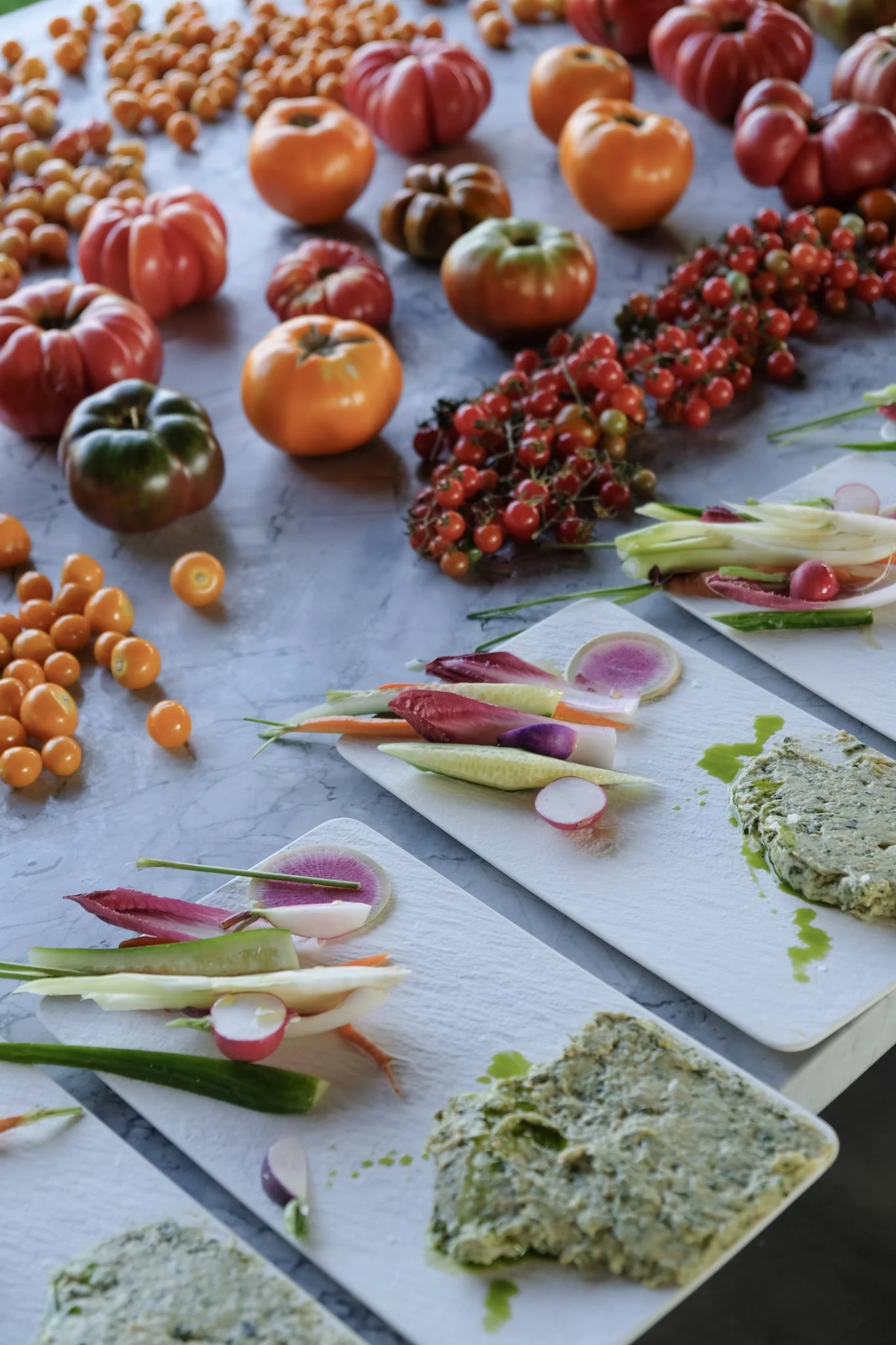 Assorted heirloom tomatoes on a table with vegetable spreads and colorful vegetable sticks on white plates.