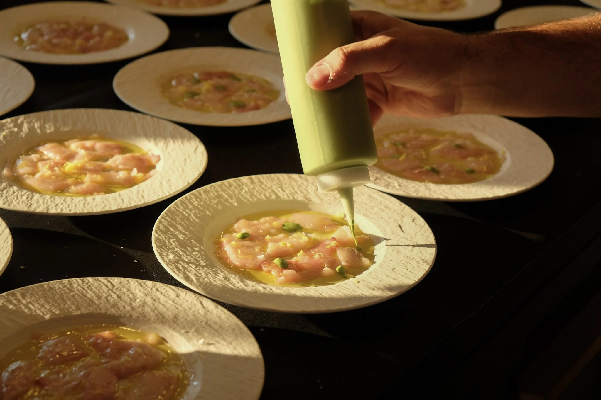Person applying green sauce to dishes of raw chicken on white textured plates.