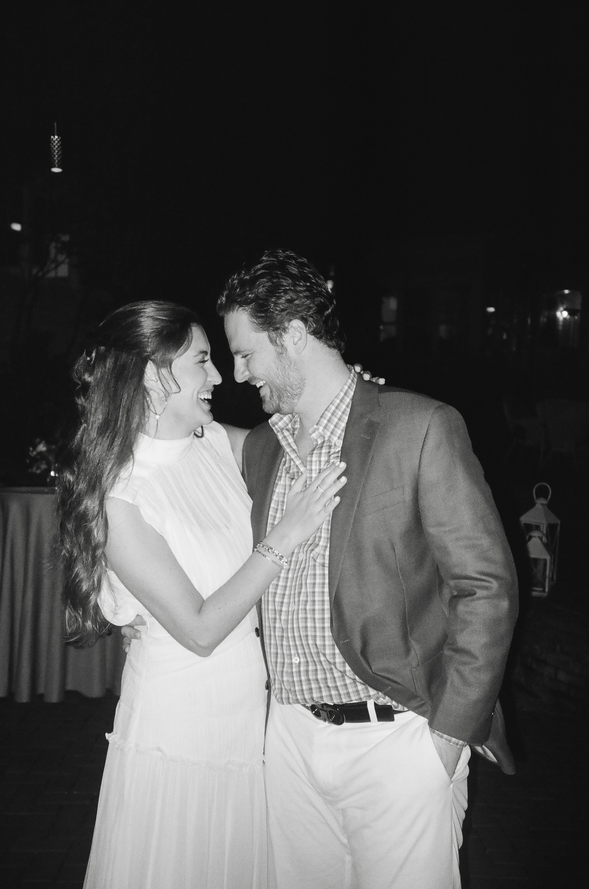 A black and white photo of a smiling woman and man close together, appearing to share a joyful moment, at night.