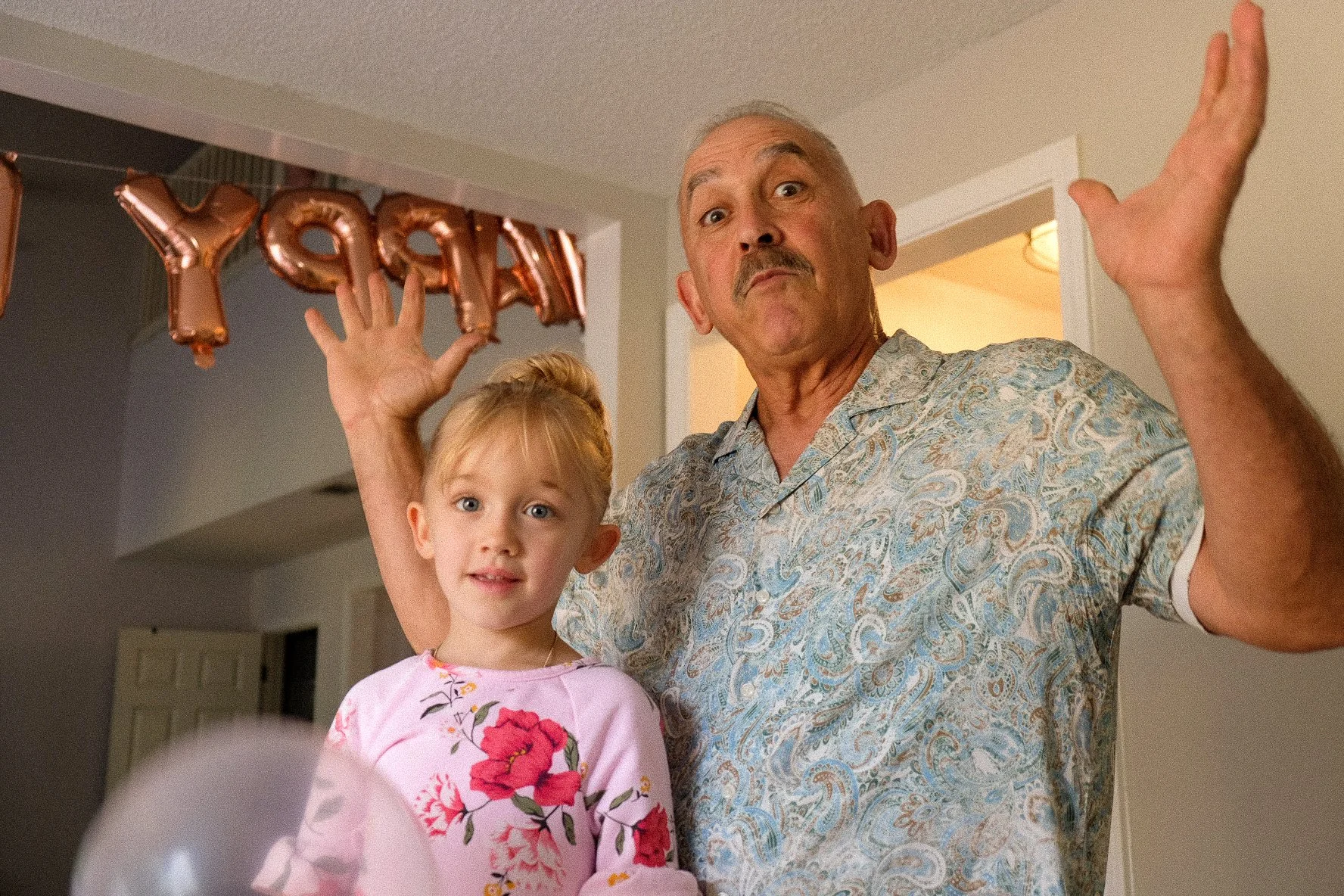 A man and a young girl celebrating birthday with balloons and a 'Happy' balloon decoration in the background.
