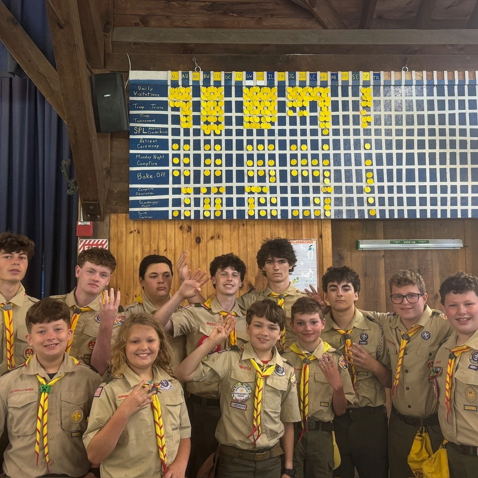 Group of boy scouts in uniform posing with a large board filled with yellow pins and a kid dominant board above them at a scouting event.  Camp Yawgoog Sandy Beach Champions 4 years in a row!