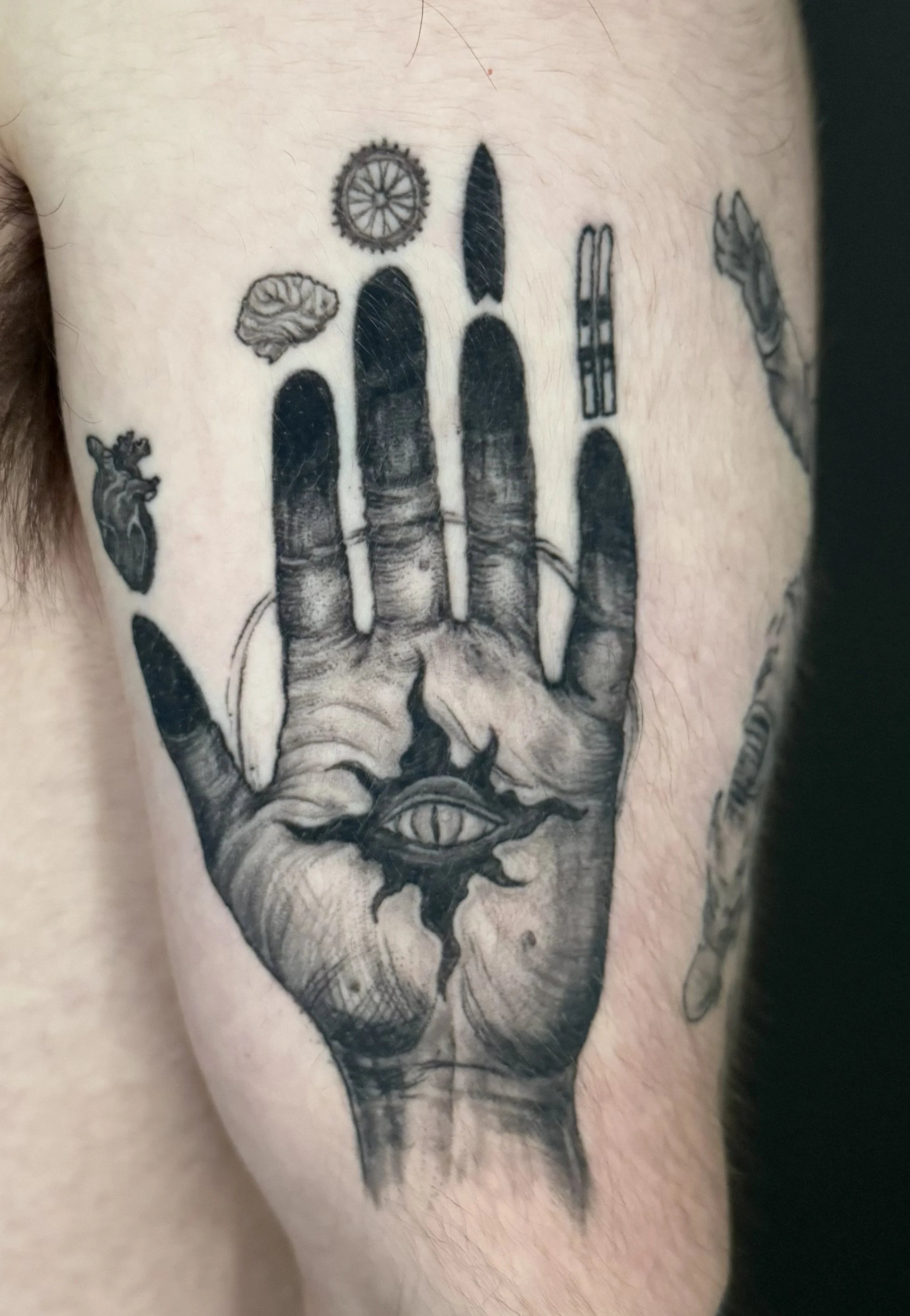 Tattoo of a hand holding a snake with a human eye on the wrist, a brain on the middle finger, a wheel on the index finger, a sword on the ring finger, and an eye on the thumb.