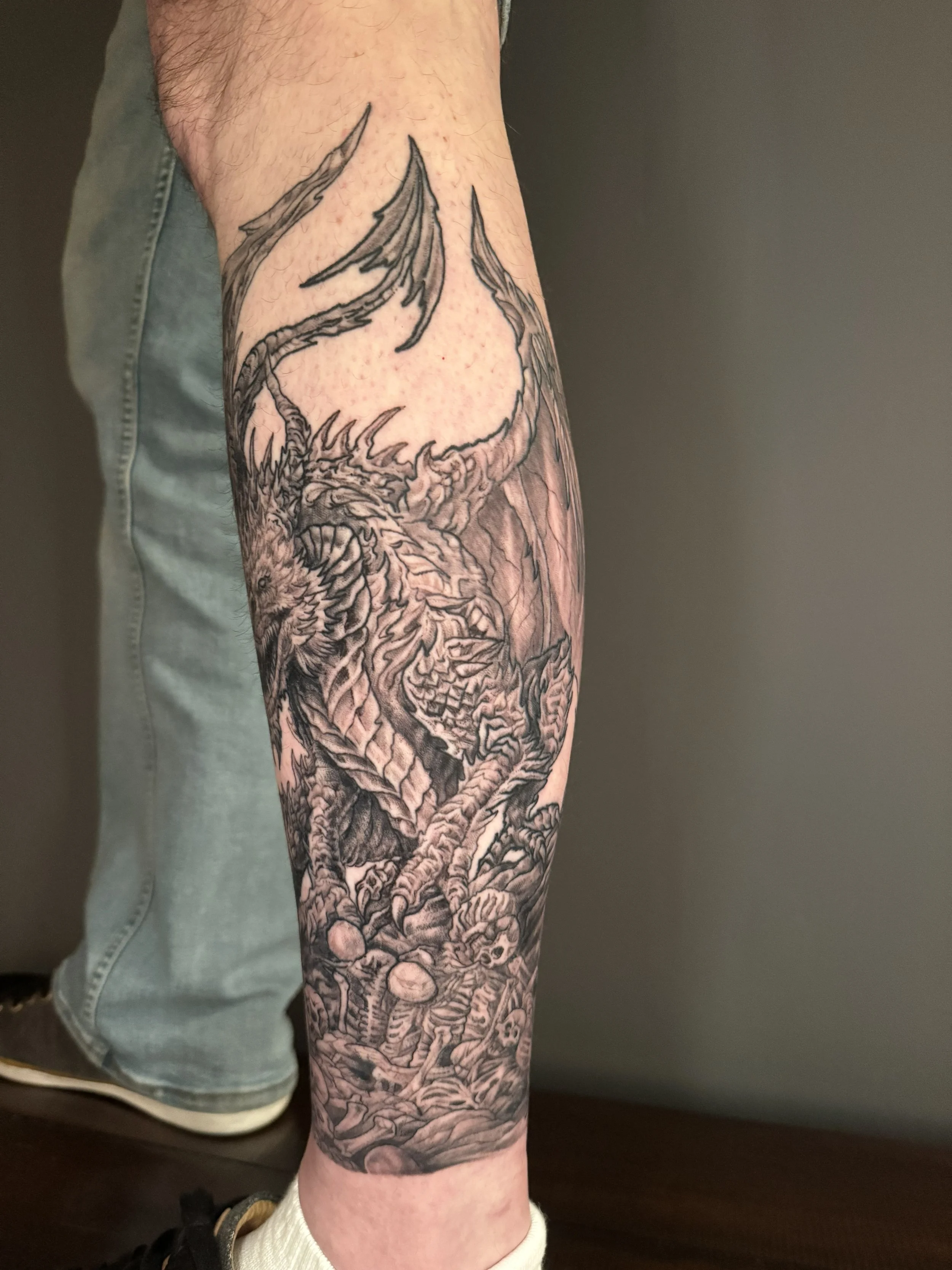 A detailed black and gray tattoo of a dragon covering the person's forearm from wrist to elbow.
