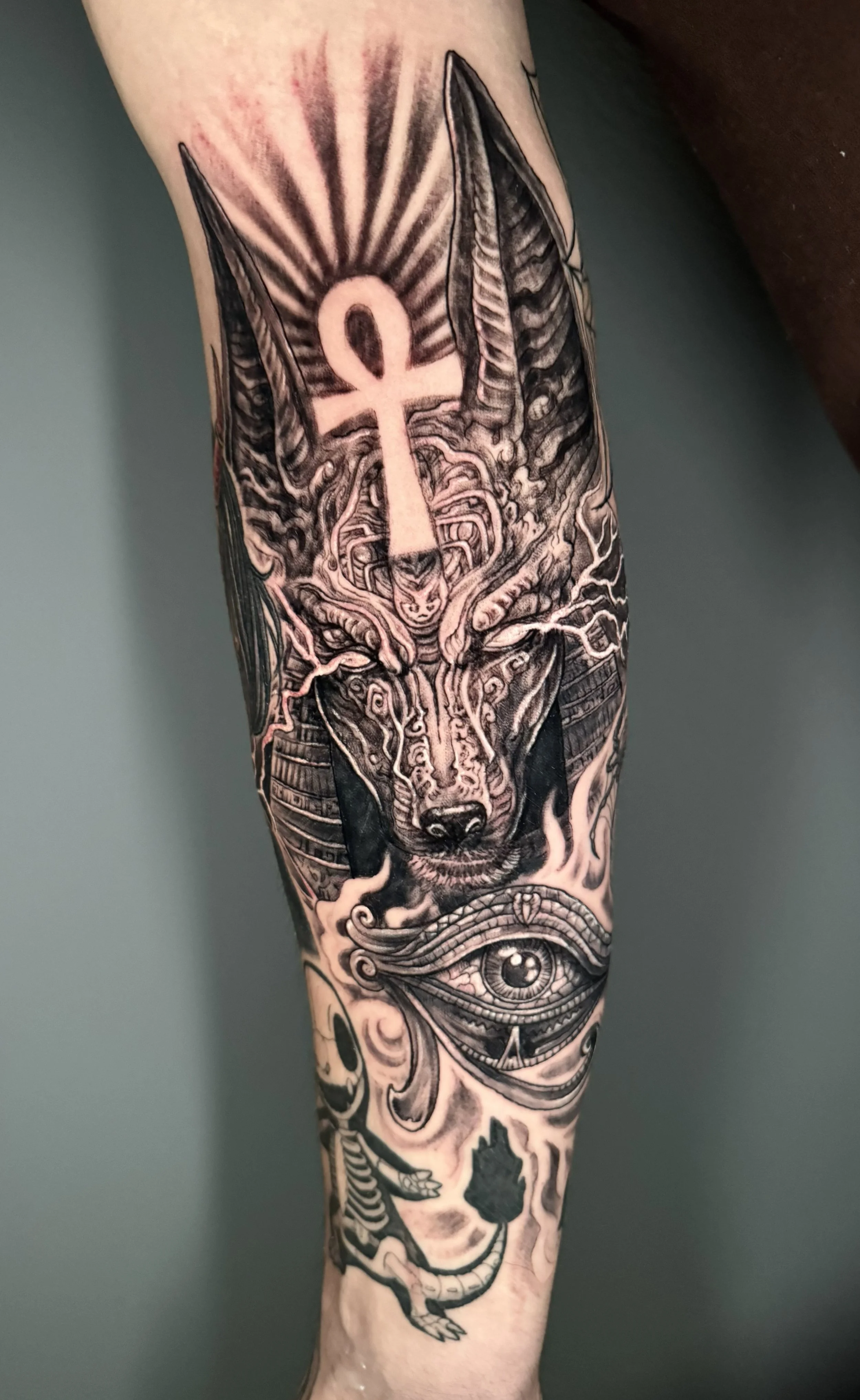 A black and gray tattoo of a wolf's head with a compass inside its forehead, surrounded by intricate designs and patterns, including an eye near the wrist.