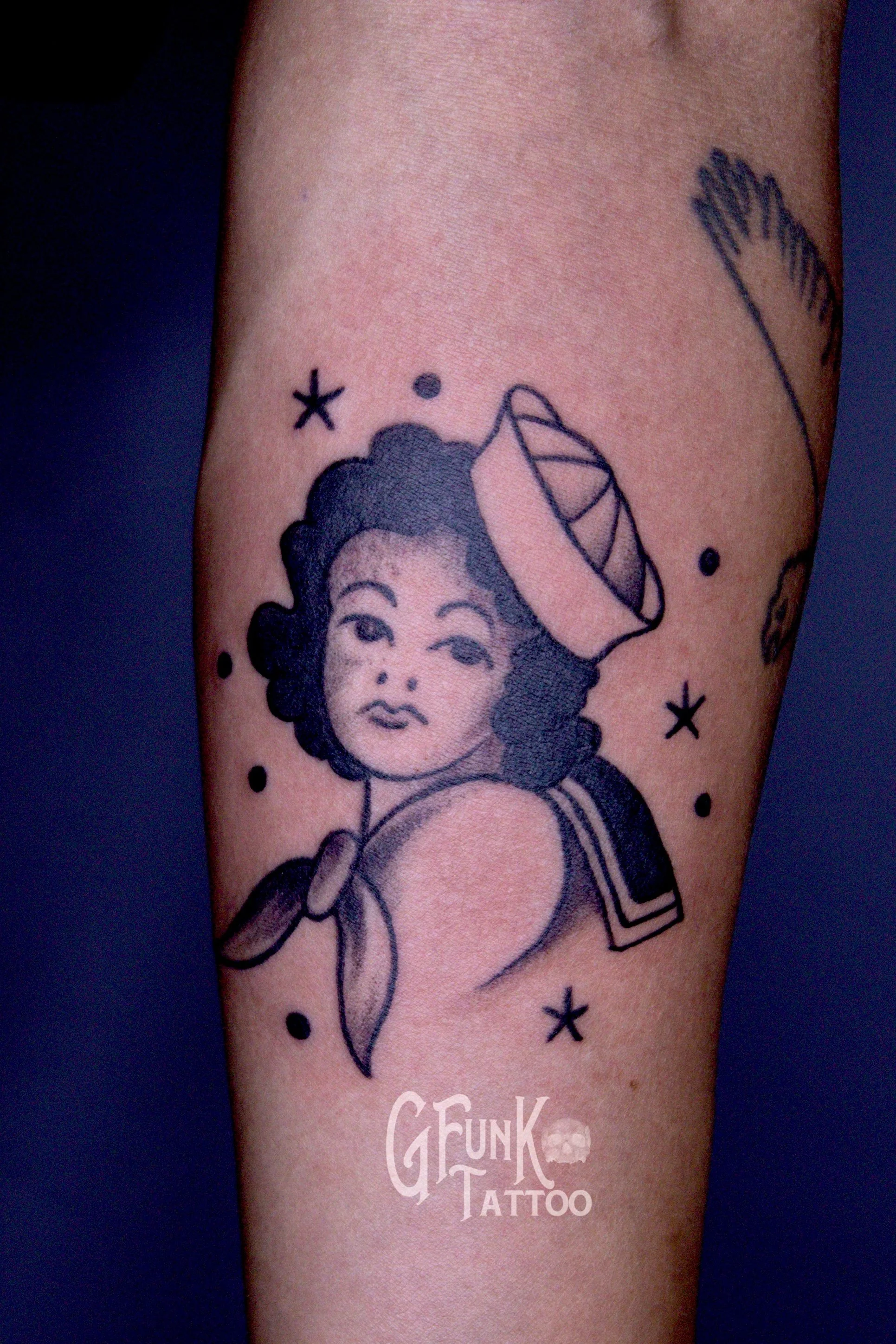 A tattoo on a person's arm depicting a woman with curly hair, a flower, and small stars and dots around her.