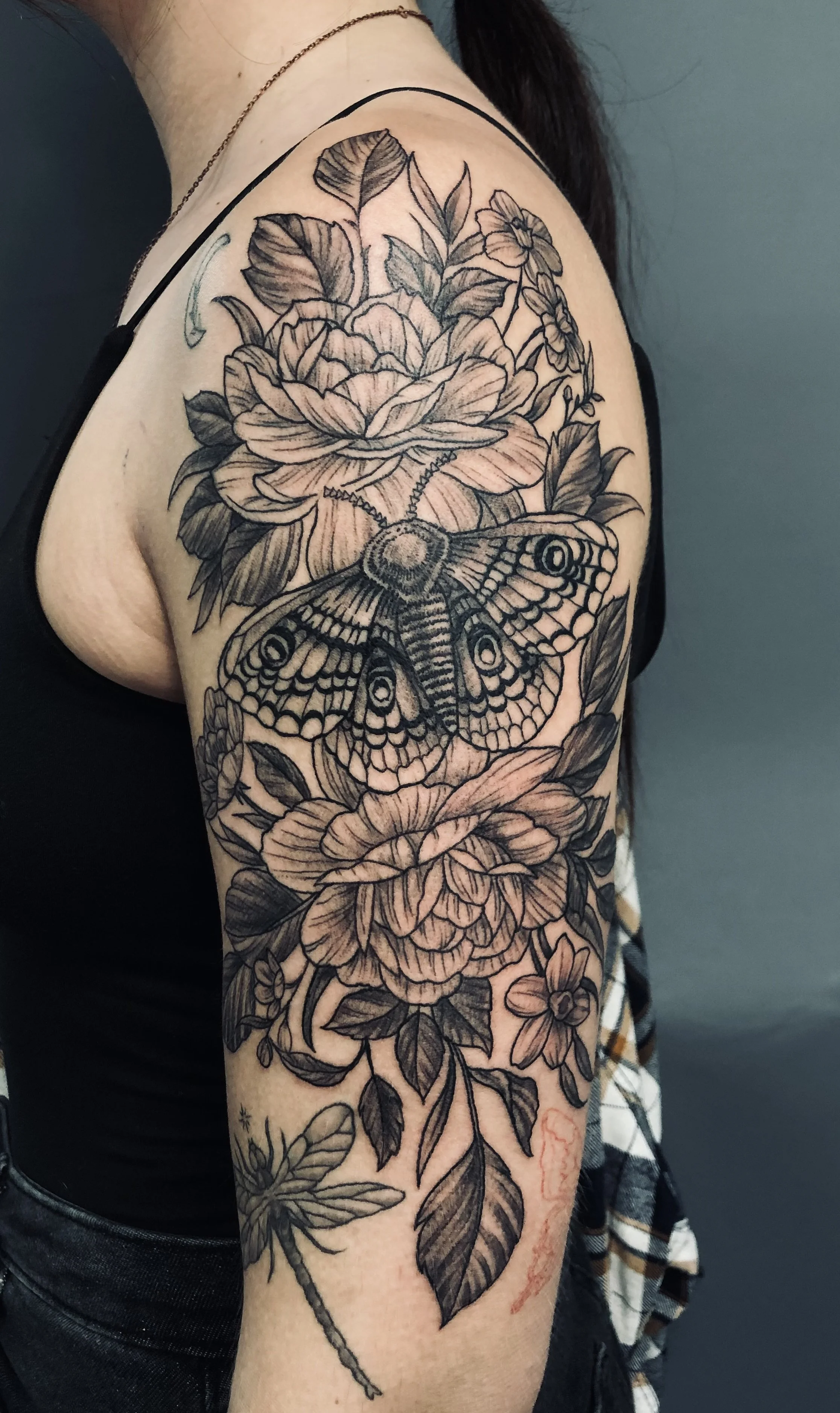 Black and gray floral tattoo with a large moth in the center on a person's upper arm and shoulder.