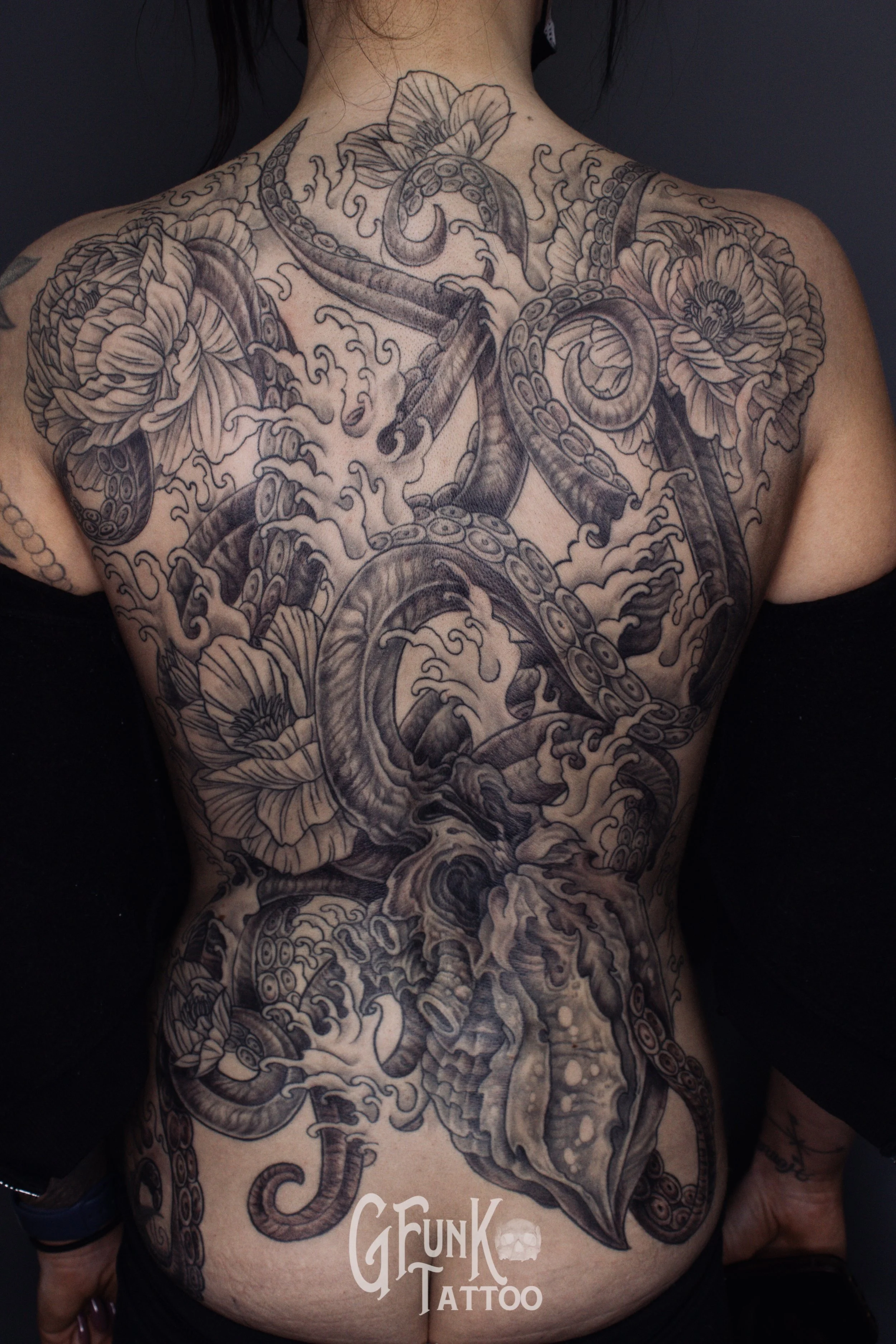 Black and gray tattoo of a coiled octopus and flowers on a person's chest and torso.