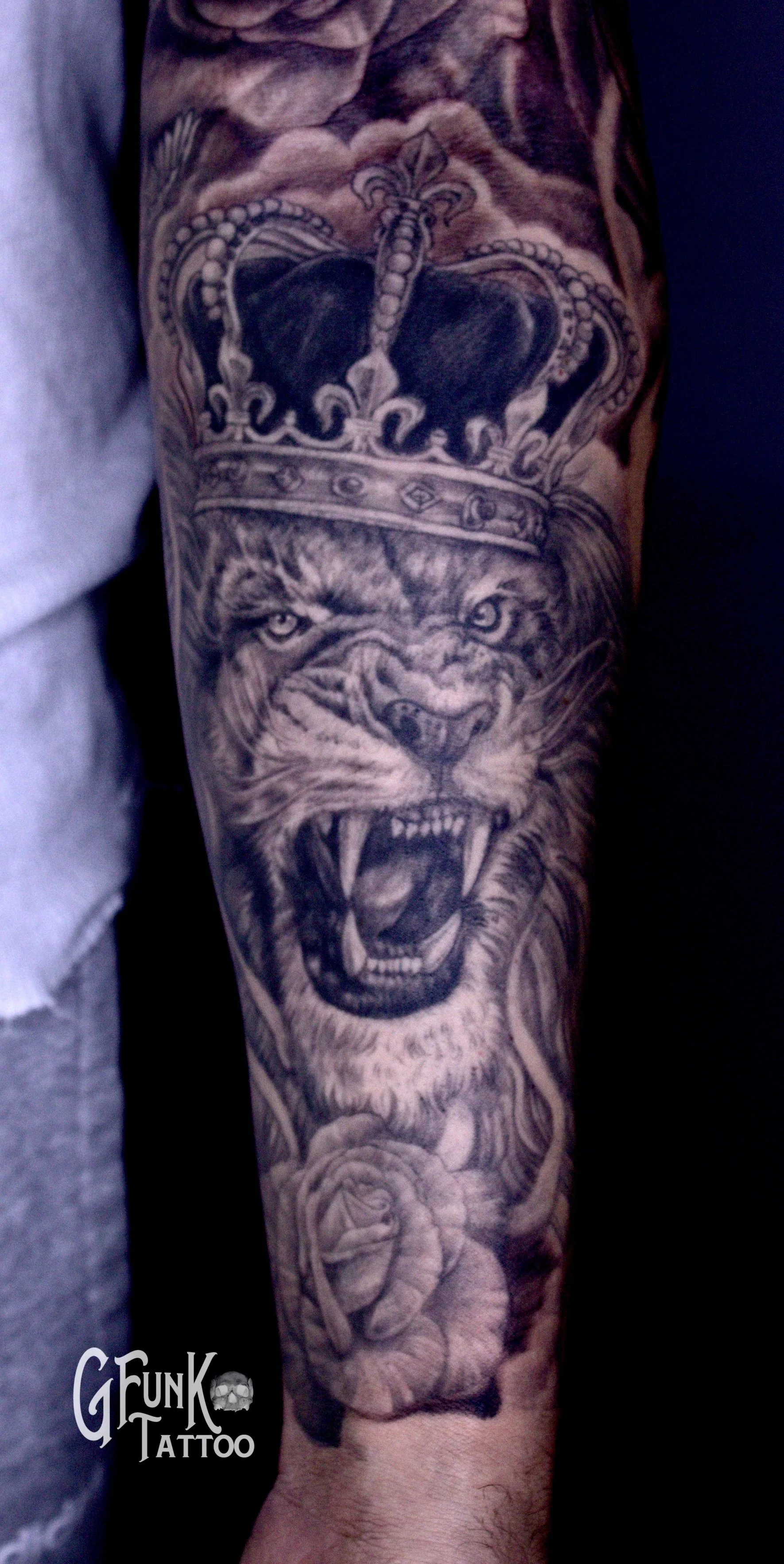 Black and gray tattoo of a roaring lion wearing a crown on a person's forearm.