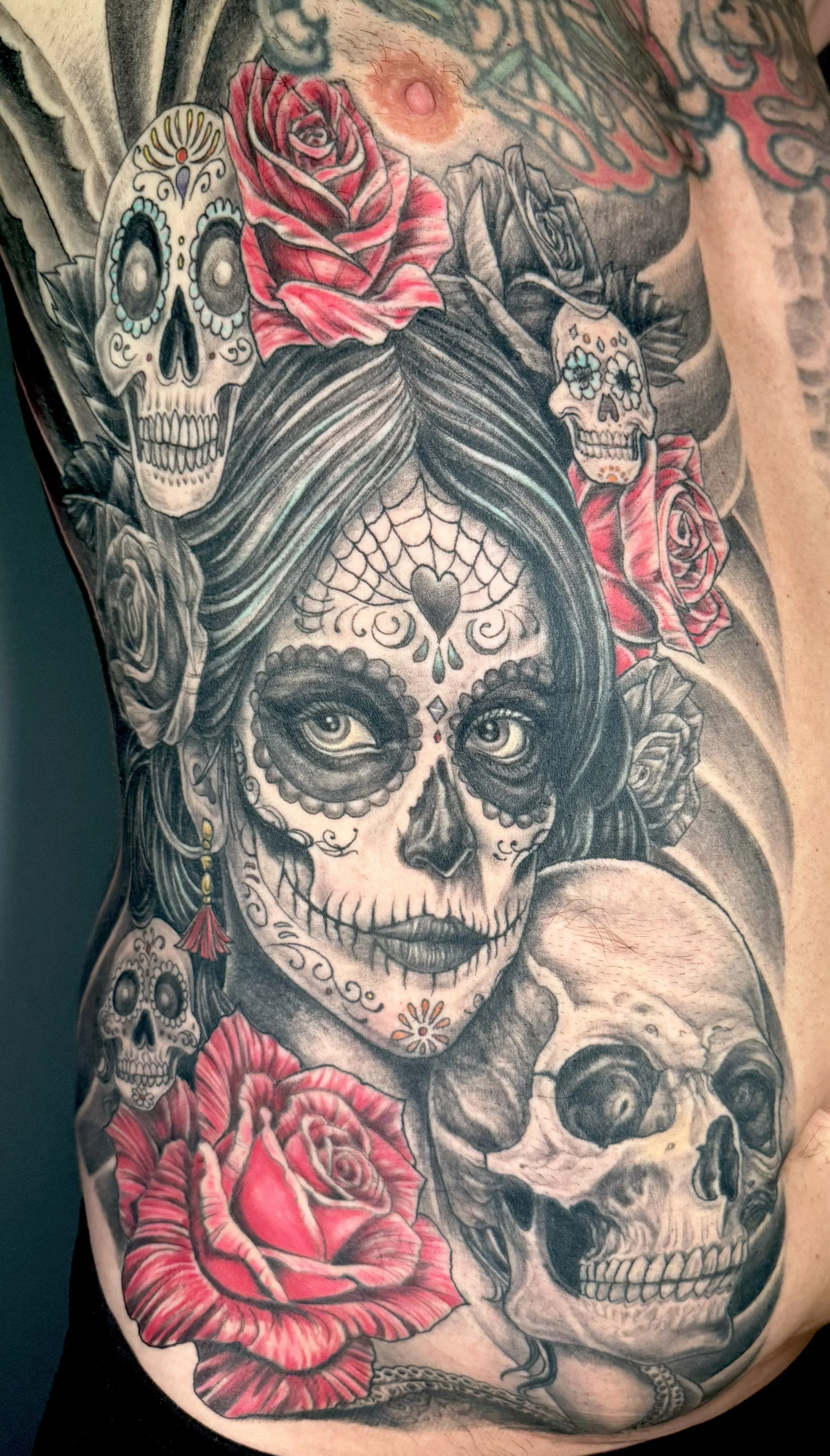 Tattoo of a woman with samba skull makeup, surrounded by roses and smaller skulls.