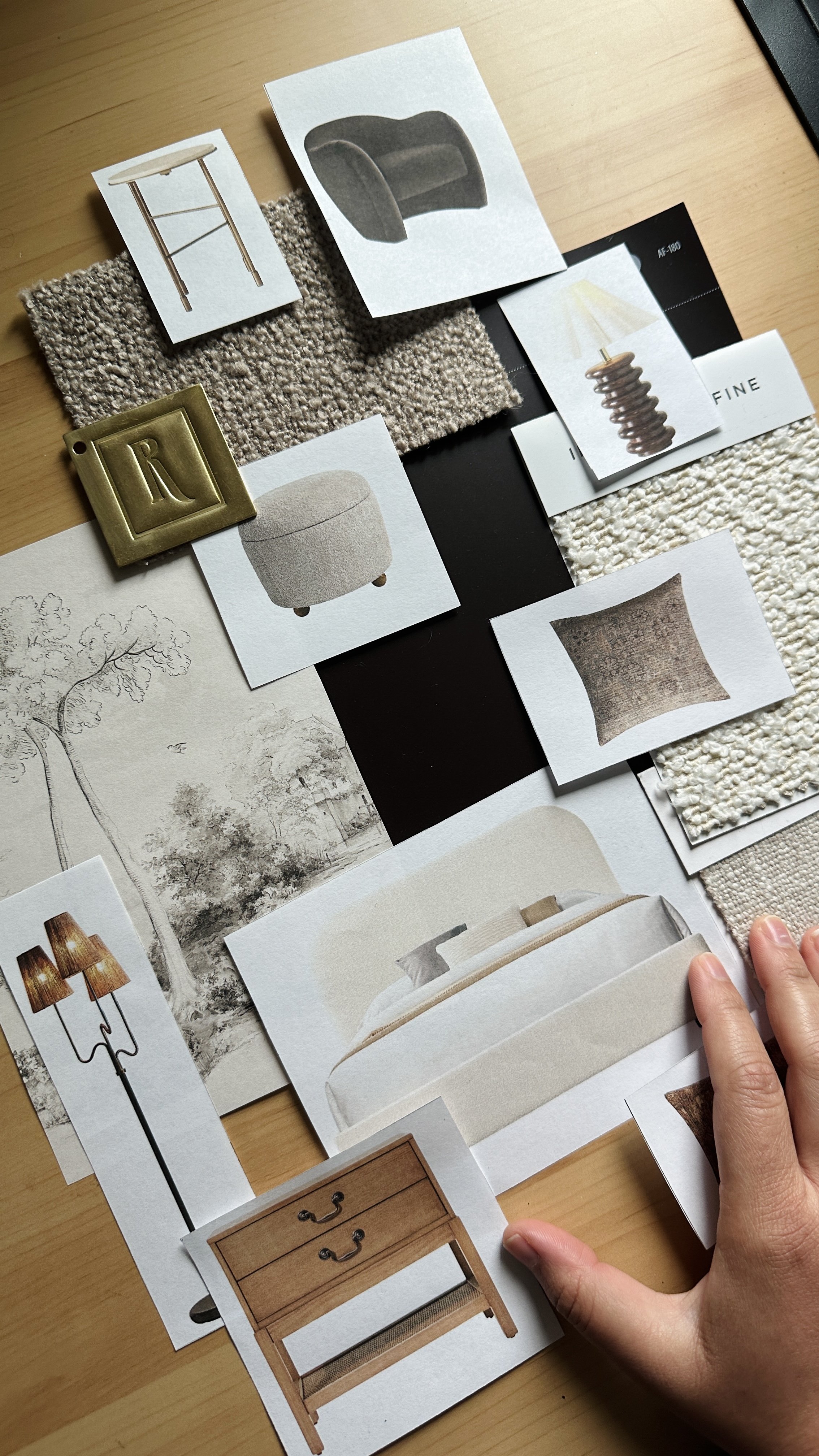 A person holding interior design magazine pages featuring furniture and decor swatches, with fabric samples, and furniture sketches on a light wood table.