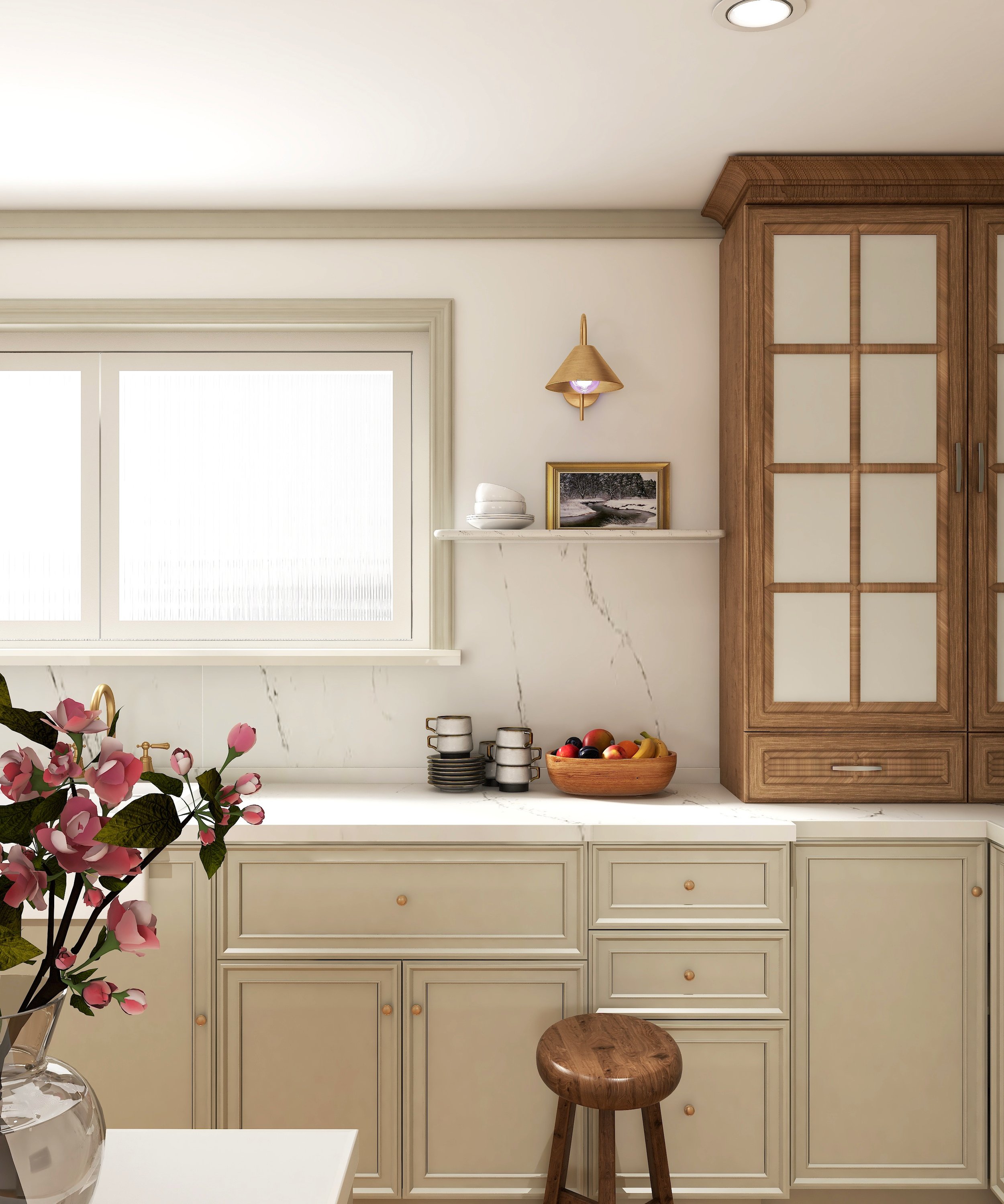 A kitchen with cream-colored cabinets, a marble countertop, and a window with blinds. On the counter, there are stacks of plates and a basket of fruit. A small wooden stool is in front of the cabinets, and a wall sconce with a gold finish is mounted above a picture frame. A pink flower arrangement is visible in the foreground.
