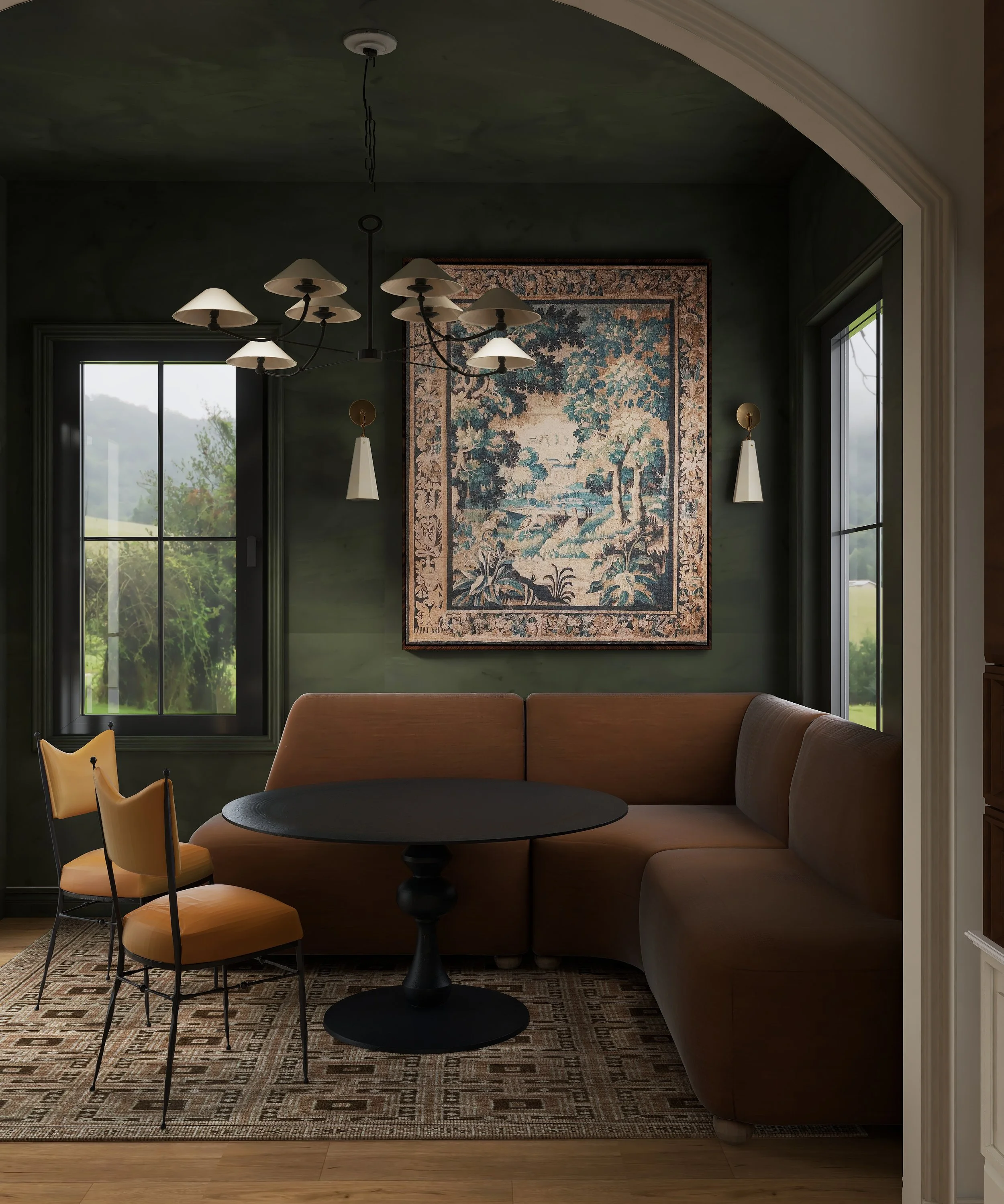 A dining room with a curved beige sectional sofa, a round black table, and orange chairs with black metal legs. The room has green walls, a large window with views of the outdoors, and a tapestry hanging on the wall. There are two wall sconces and a modern chandelier with multiple cream-colored shades hanging from the ceiling.
