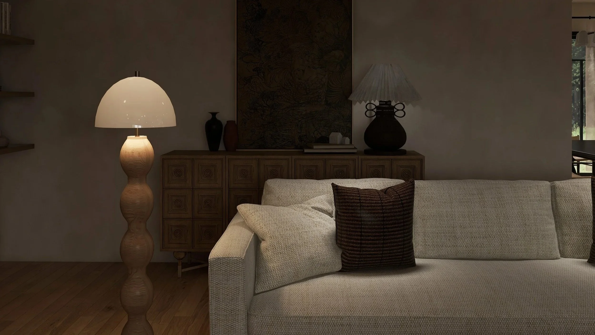A dimly lit living room featuring a beige sofa with textured fabric, decorative pillows, a wooden sideboard with black and brown vases and small white decorative objects, a tall artistically carved wooden floor lamp with a white shade, and a framed large dark artwork hanging on the wall behind the sideboard. There is also a window on the right side with a view of greenery outside.