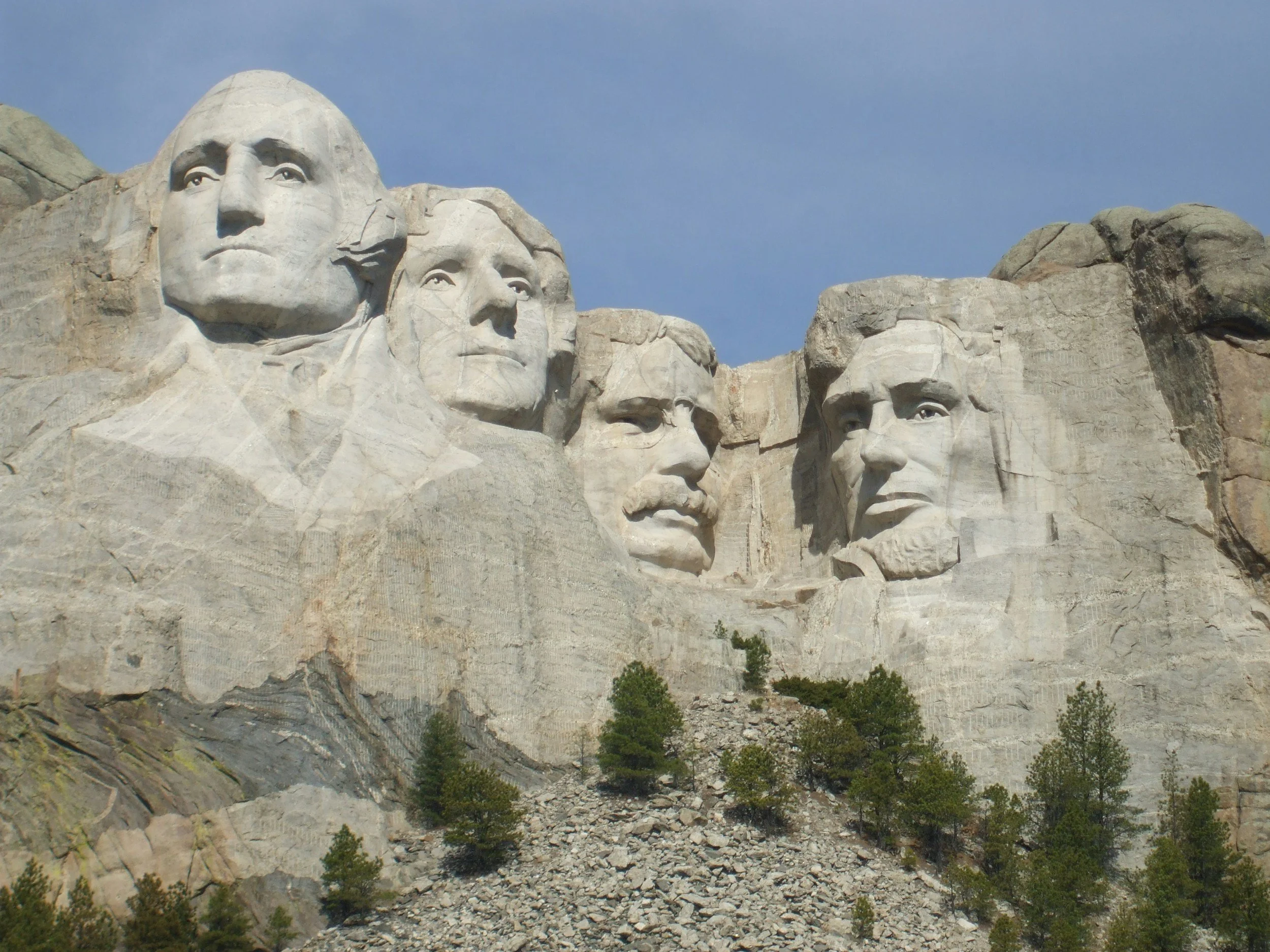 Mount Rushmore with carved faces of four U.S. presidents in the granite mountain, surrounded by trees and a clear sky.