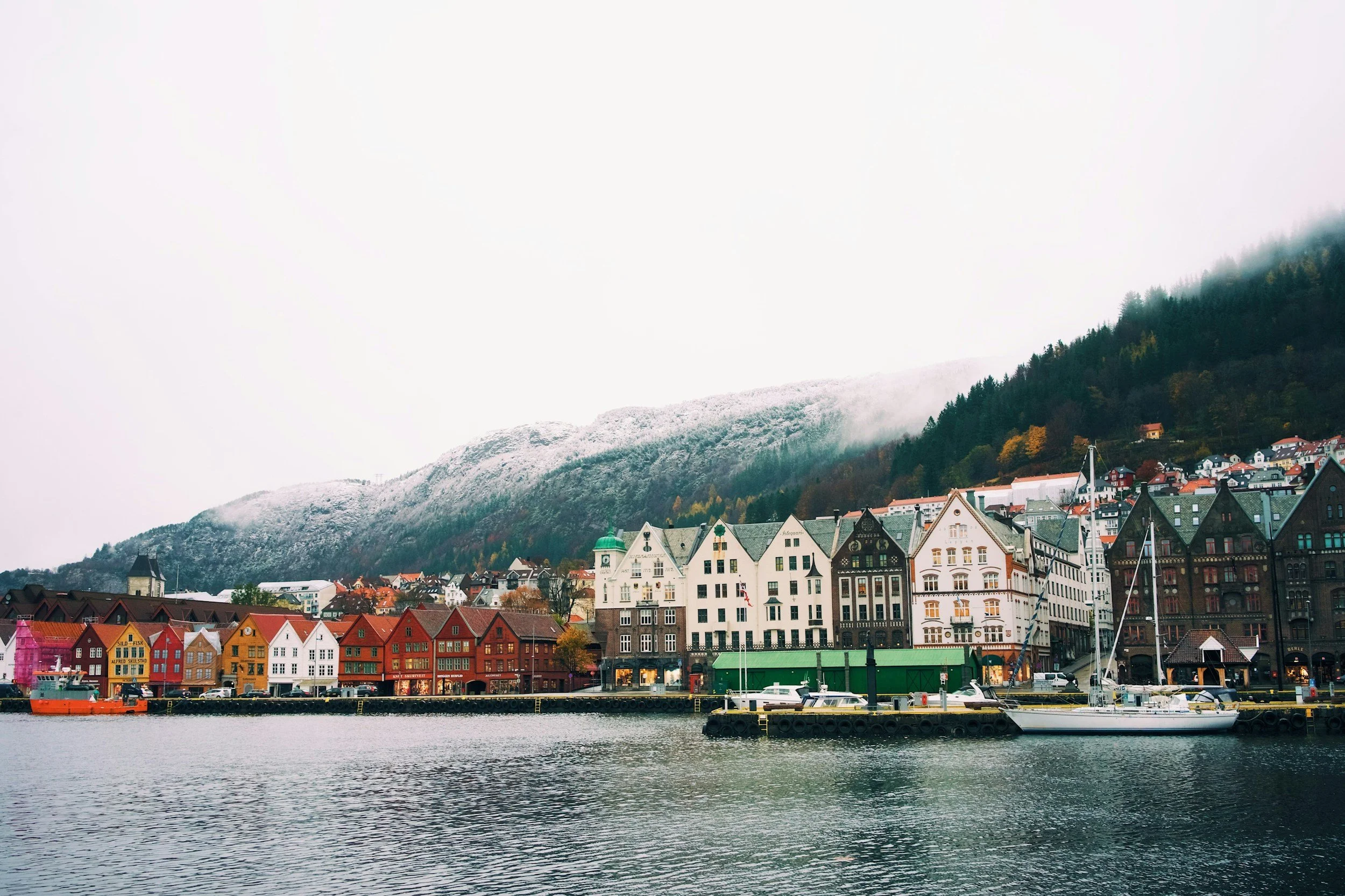 Colorful buildings and boats along a waterfront with snow-capped mountains in the background.