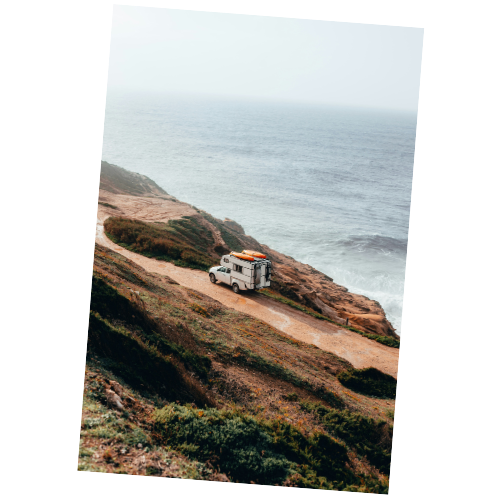 A camper van parked on a dirt road along a cliff overlooking the ocean, with cliffs covered in grass and low shrubs.