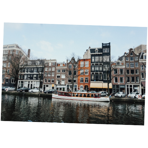 Row of colorful historic buildings along a canal in Amsterdam with a boat passing by.