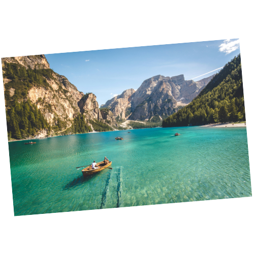 A boat floating on a clear, turquoise lake surrounded by mountains and dense green trees under a blue sky.
