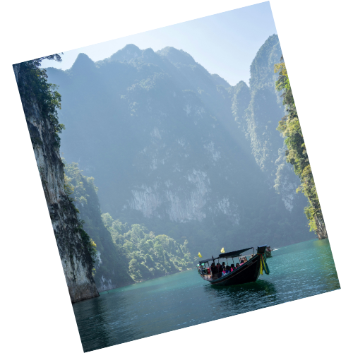 A boat with people sailing on a river surrounded by tall, lush green mountains with cliffs.
