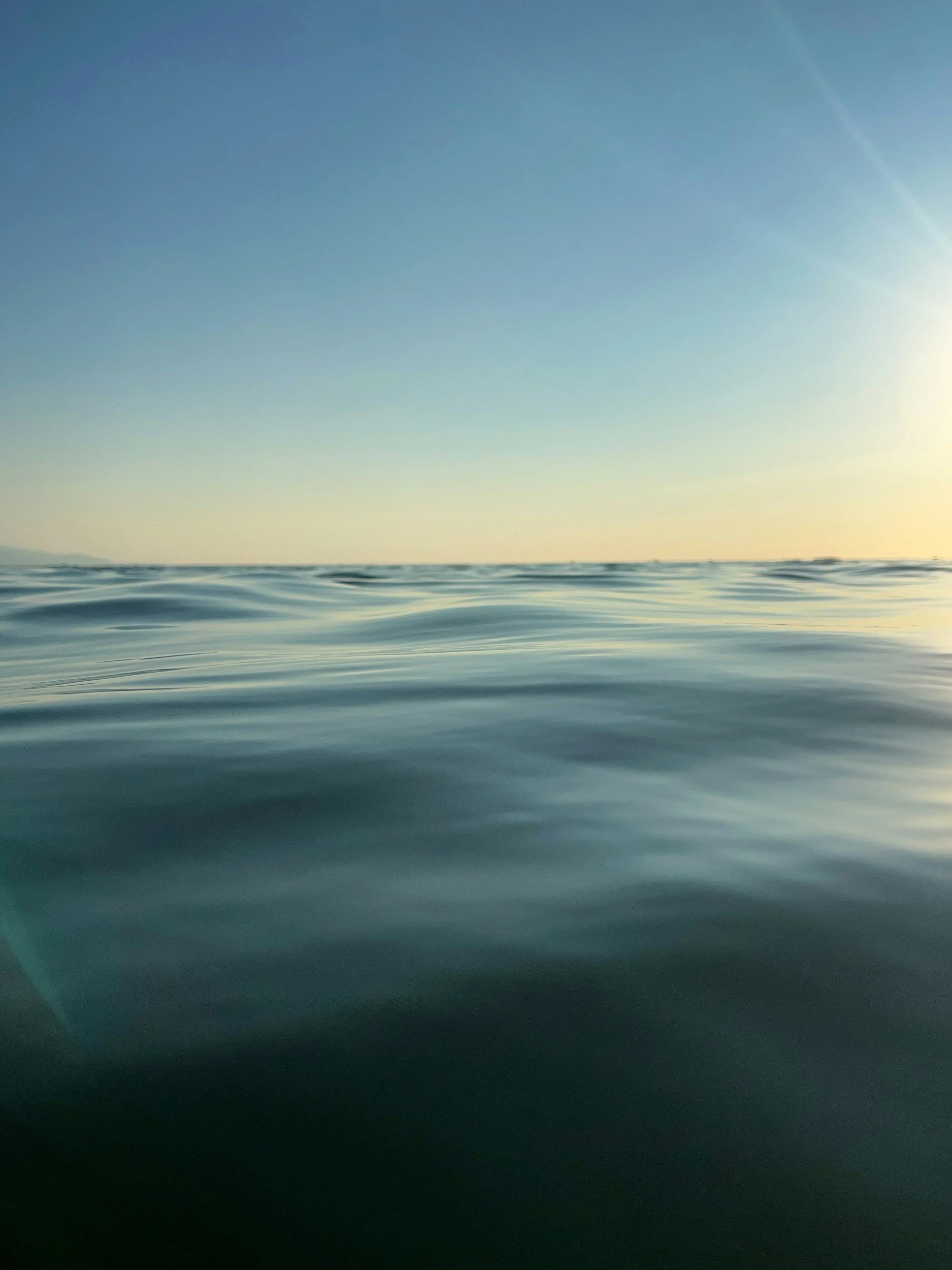 Calm ocean water with gentle ripples and a clear sky at sunrise or sunset.