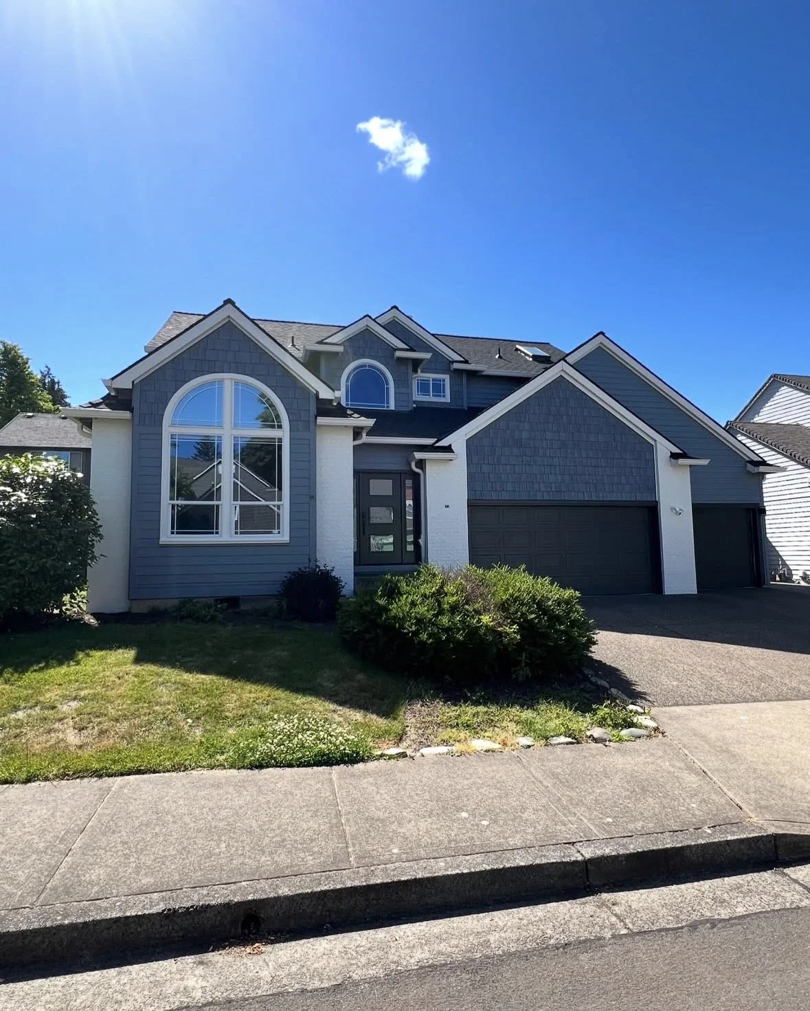 A modern two-story house with blue siding, large arched window, and attached garage, under a bright blue sky with a single small cloud.