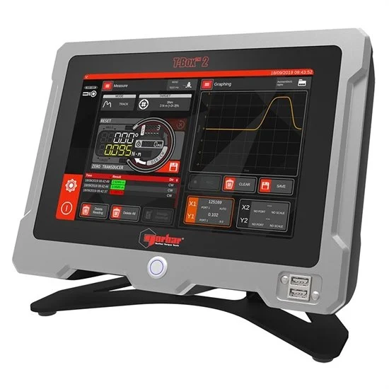 Electronic testing device with digital display showing graphs and measurements, housed in a gray case with a stand.