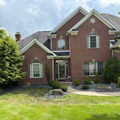 Front view of a two-story brick house with a well-maintained lawn and surrounding bushes.