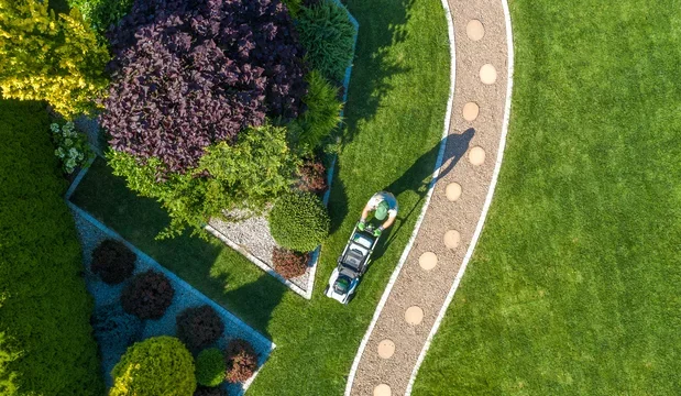 A white police car parked on a curved pathway in a garden with various trees, bushes, and grass.
