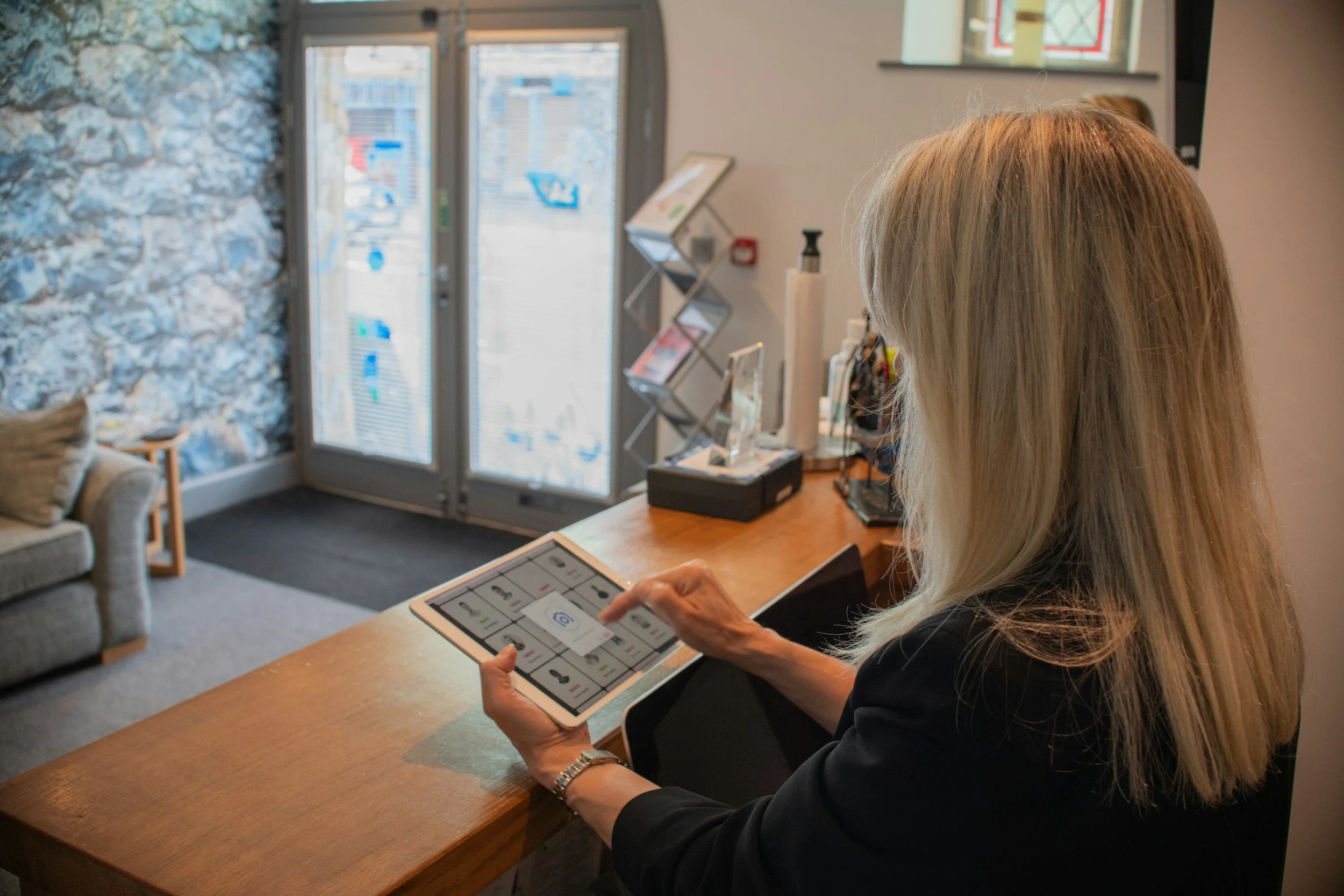 A woman with blonde hair using a tablet at a reception desk in a cozy interior.