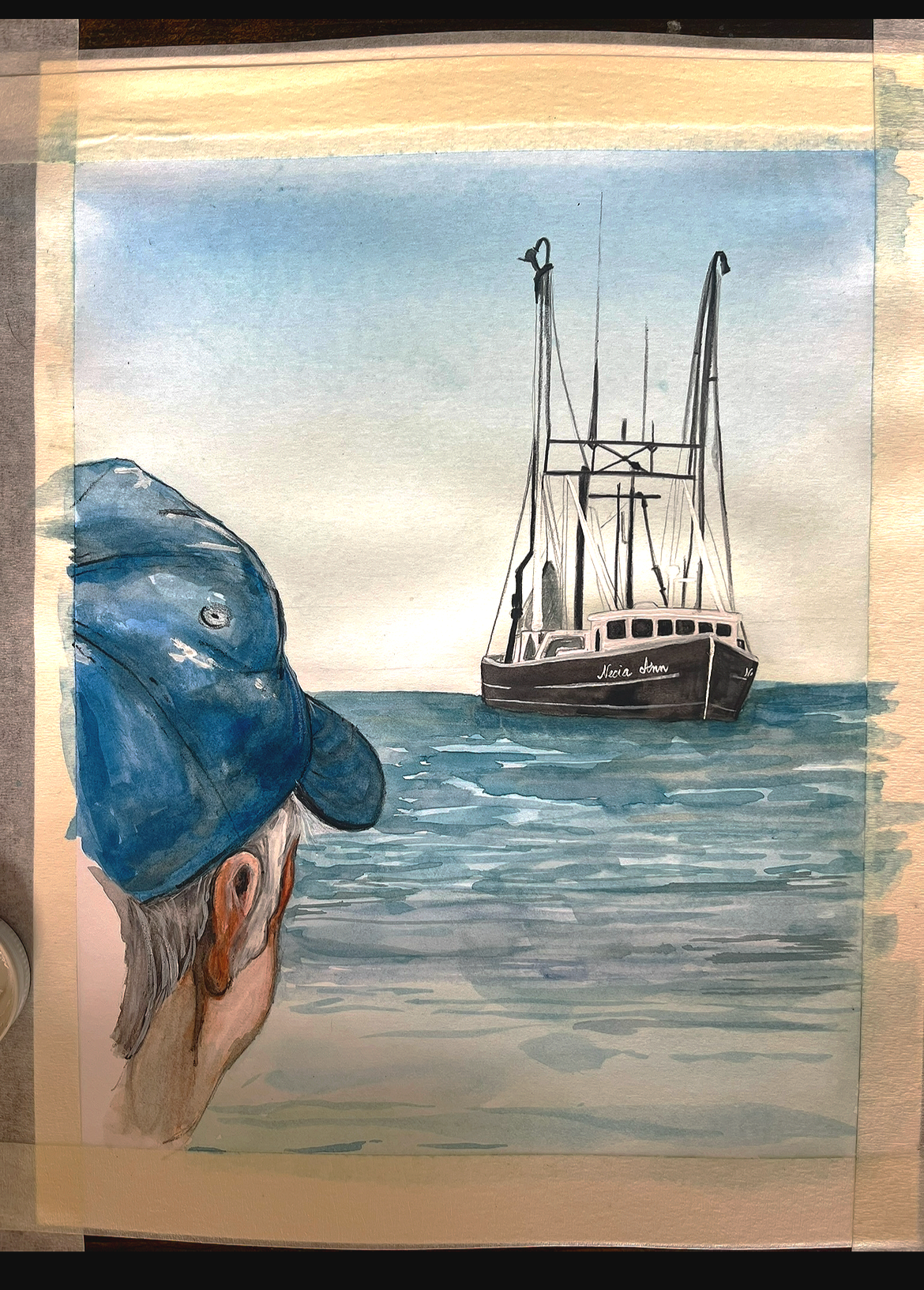 A person wearing a blue cap looks at a sailboat named 'Maria Ann' on calm water during sunset or sunrise.