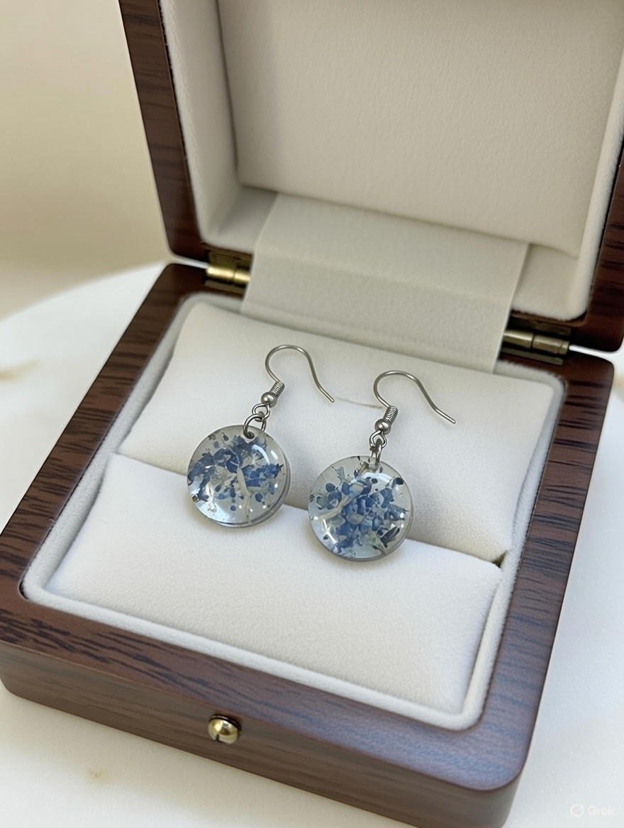 Silver earrings with circular, transparent pendants containing blue and white floral patterns in a brown wooden jewelry box.