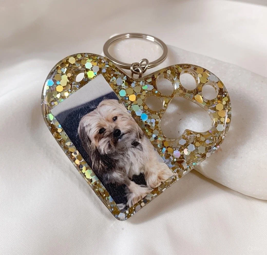 Heart-shaped glittery keychain with a photo of a small, fluffy dog attached.