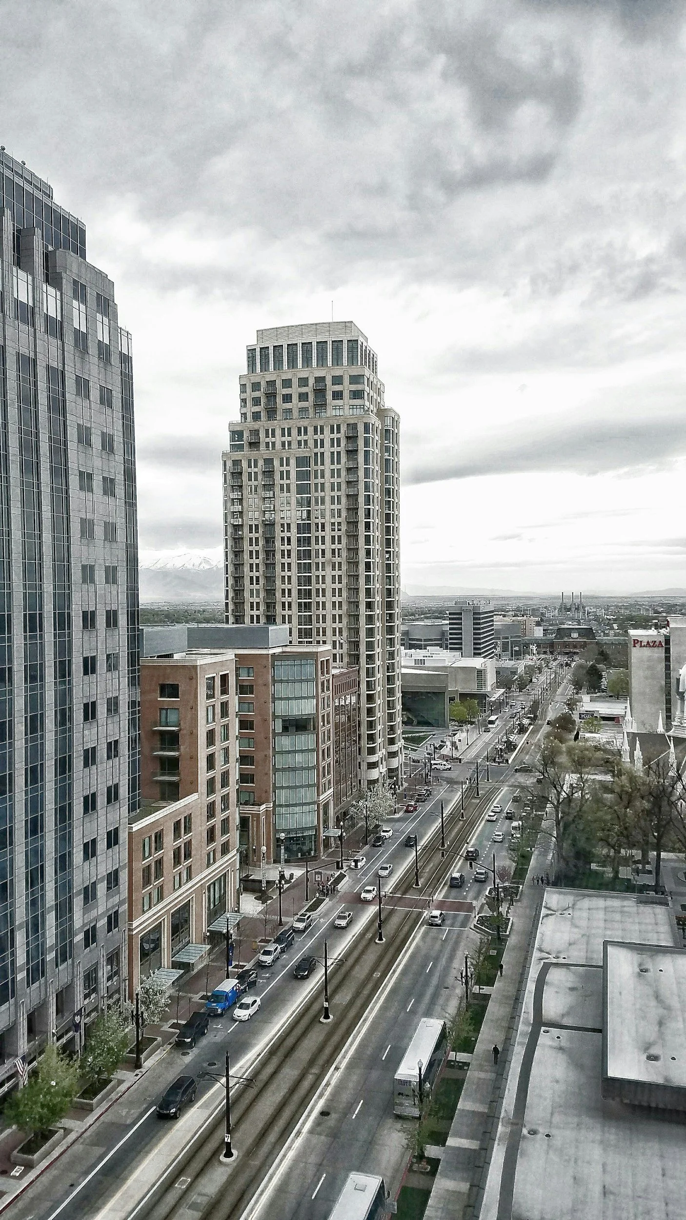 Urban cityscape with tall buildings, busy streets with cars and pedestrians, and cloudy sky.