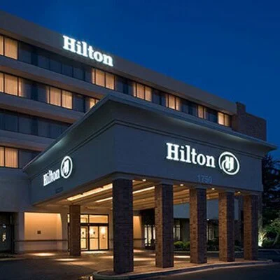 Exterior view of a Hilton hotel at night with illuminated signage and entrance