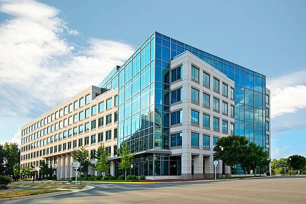 Modern office building with glass windows and trees in front, under a partly cloudy sky.