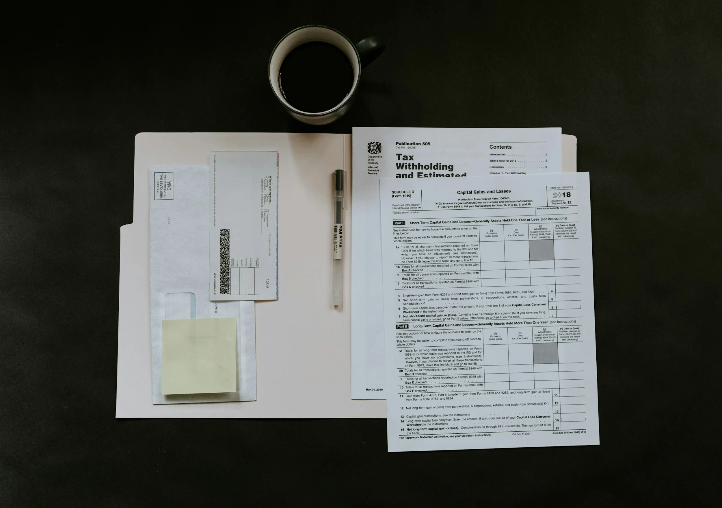 Top view of a black desk with a cup of black coffee and a tax document with a pen on it.
