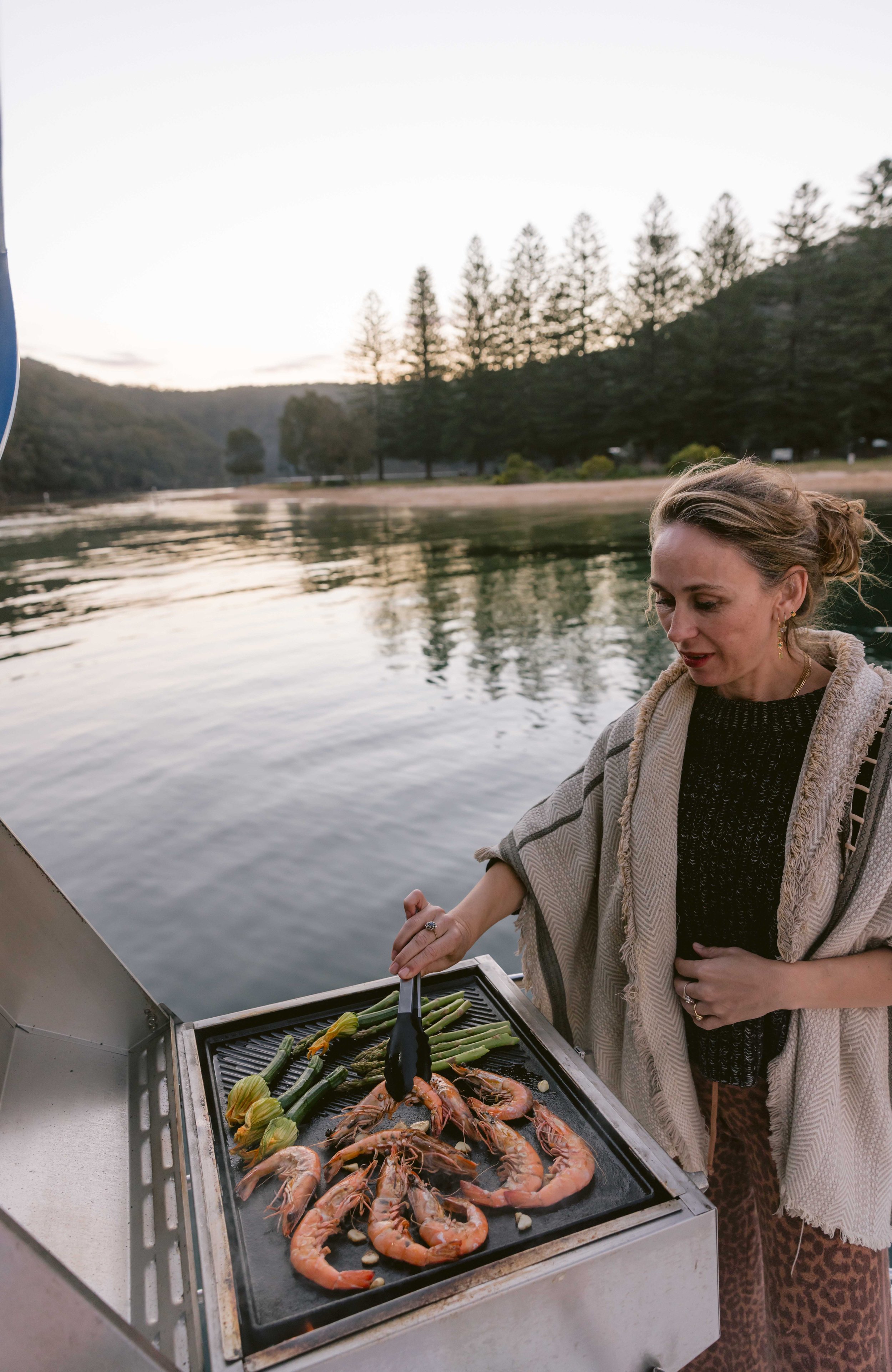 Woman cooking seafood on a barbecue grill outdoors near The Basin, Pittwater. Church Point Charter self-drive charter boat hire