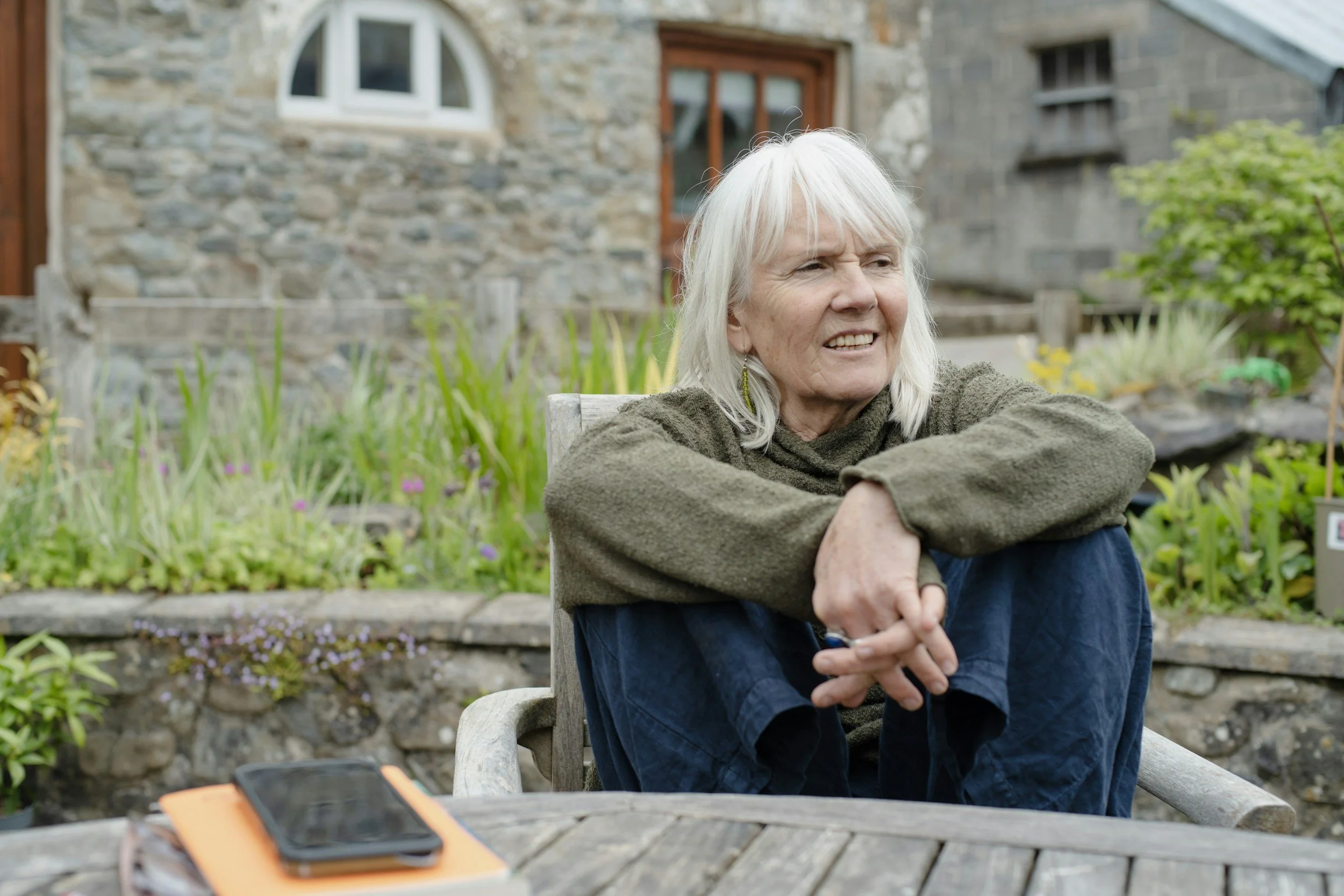 Woman with grey hair sitting outside at a wooden table pondering on life